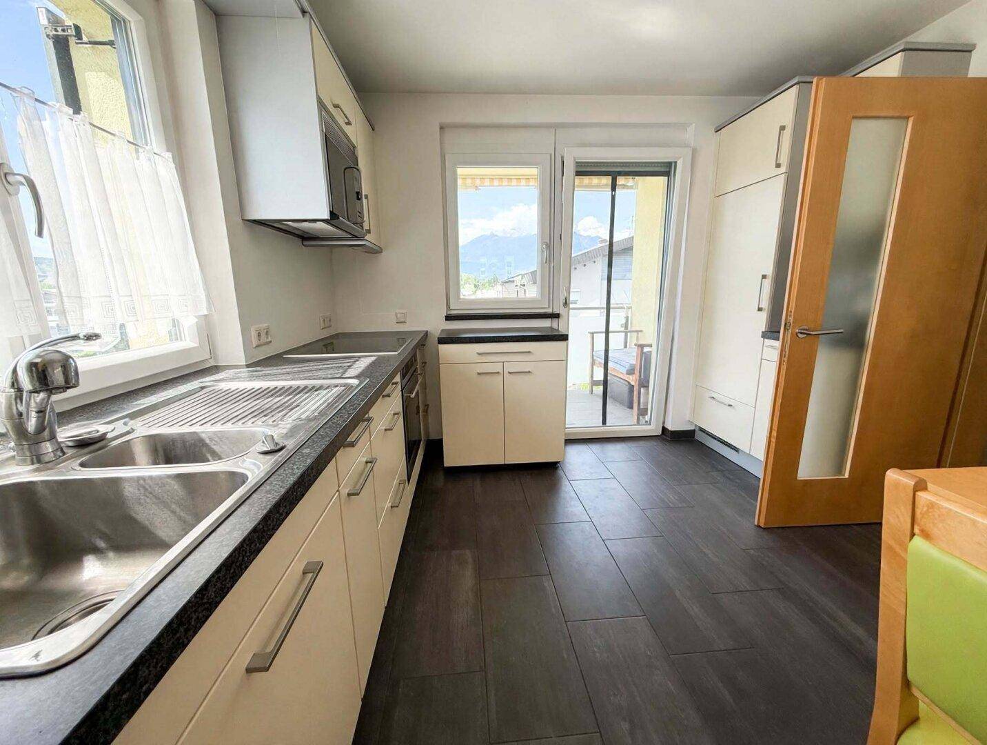 Helle Küche mit Einbauschränken, dunkler Arbeitsplatte und Zugang zu einem Balkon mit Bergblick.