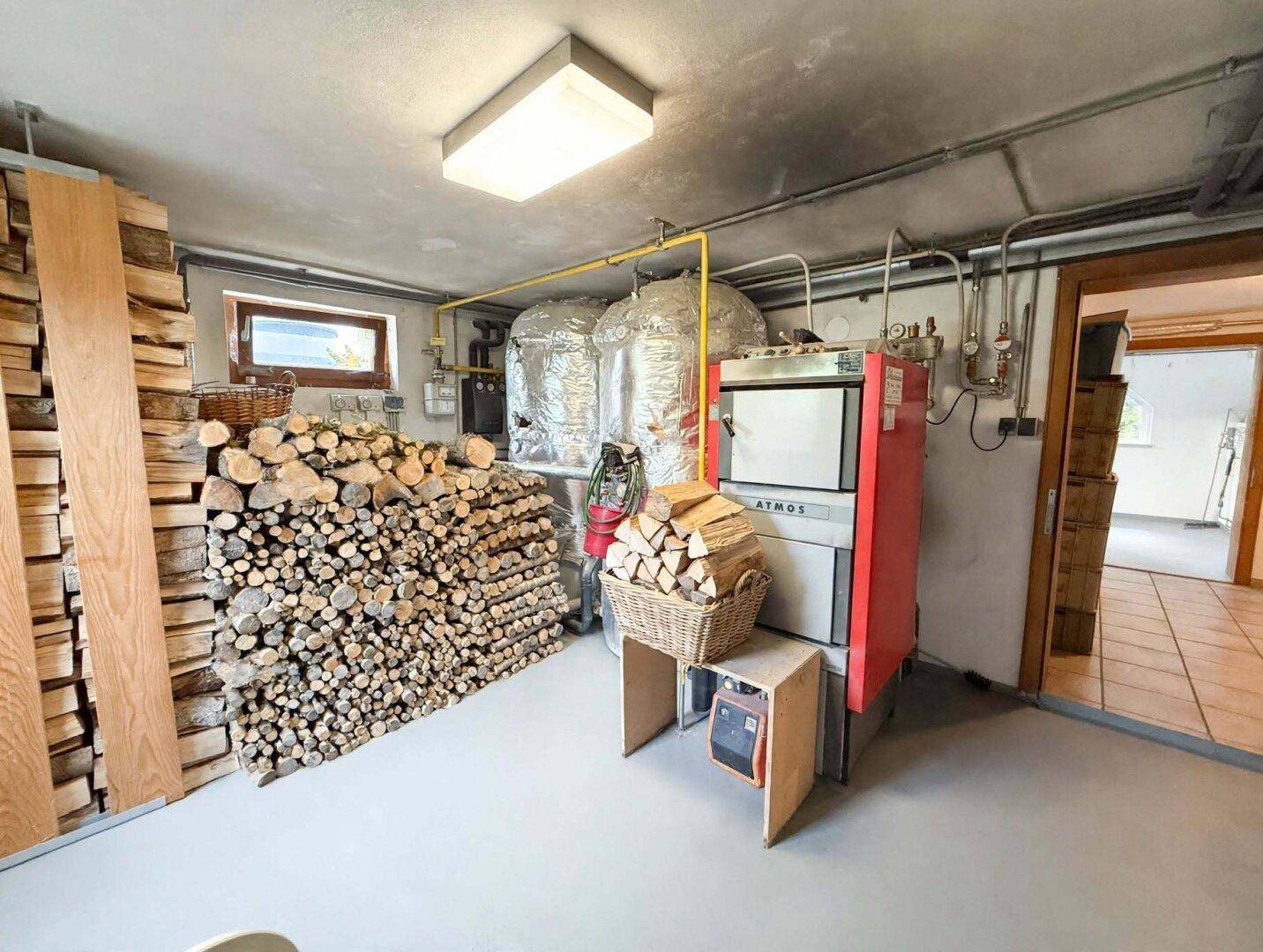 Heizraum im Keller mit Holzheizung, gestapeltem Brennholz und Lagertanks, für effiziente Wärmeversorgung.