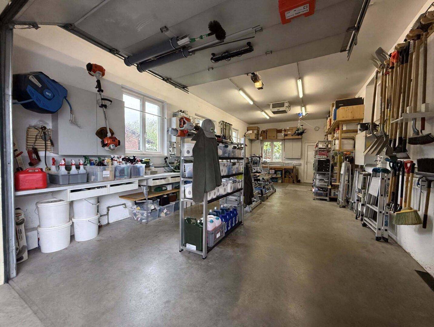 Geräumige Garage oder Werkstatt mit Betonboden, Werkzeugen und Regalen, ideal für Hobby und Lagerung.