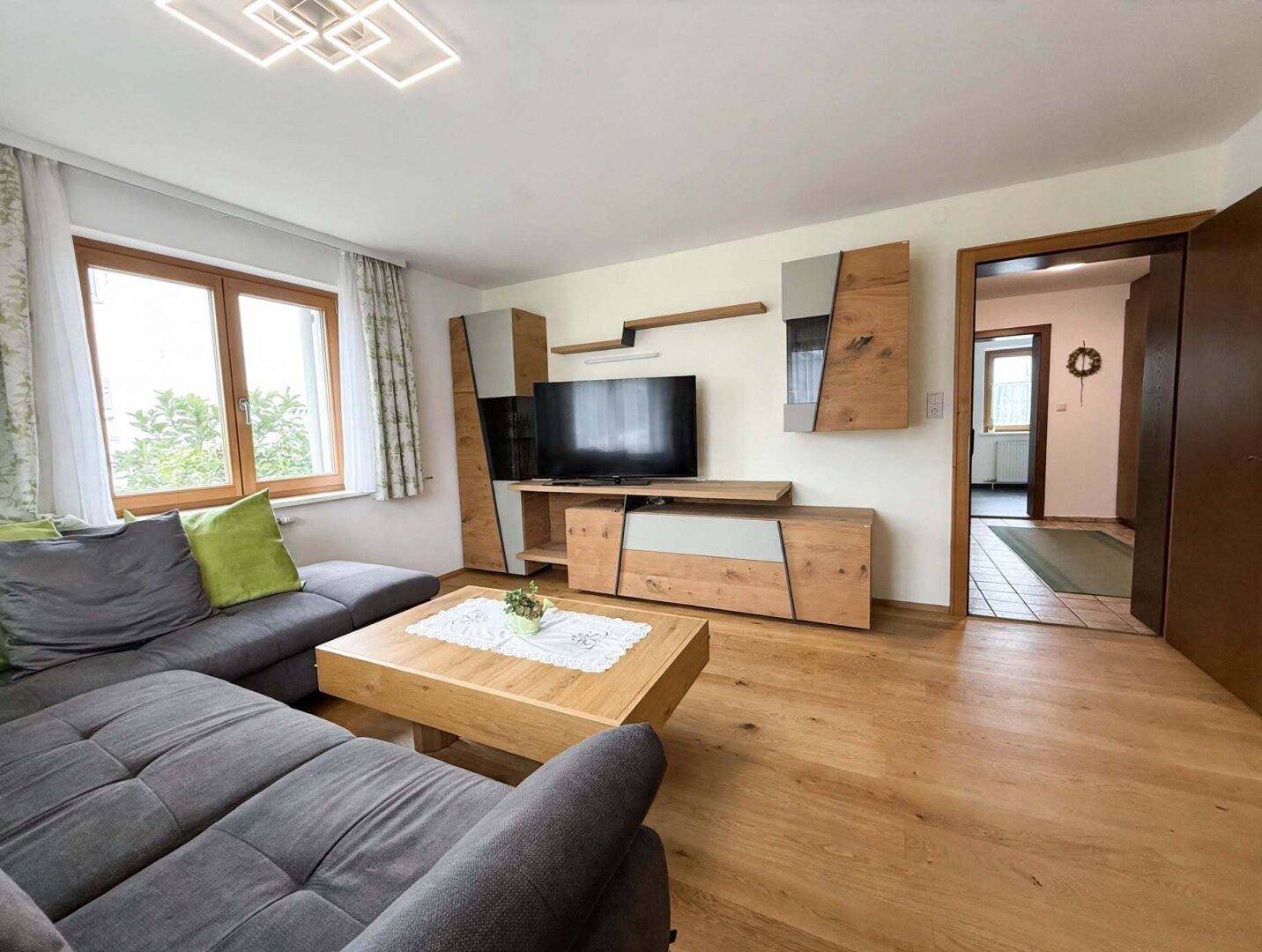 Modernes Wohnzimmer mit grauem Ecksofa, Holztisch und zeitgemäßer Wohnwand, auf hellem Holzboden.