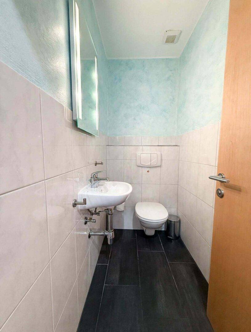 Modernes Gäste-WC mit wandhängendem WC, kleinem Waschbecken und blauen Wandakzenten.