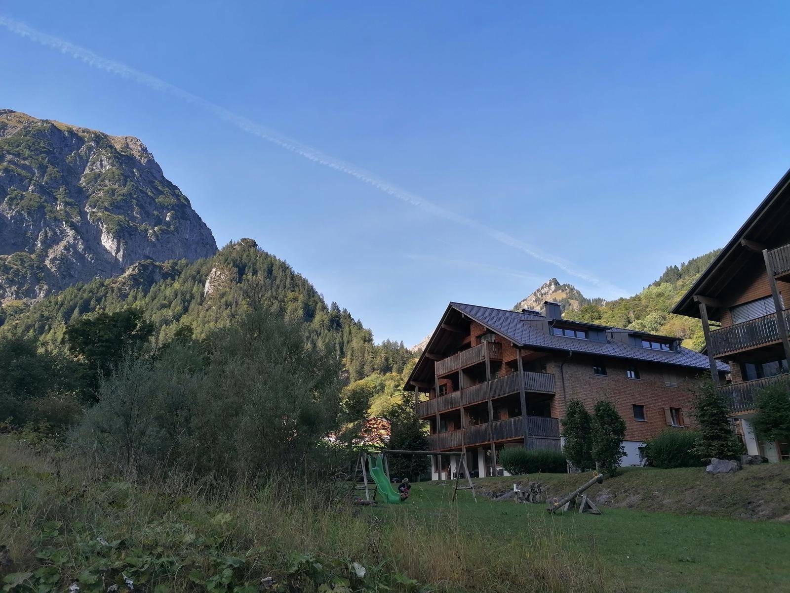 Chalet-Gebäude in grüner Berglandschaft mit Spielplatz im Vordergrund an einem sonnigen Tag.