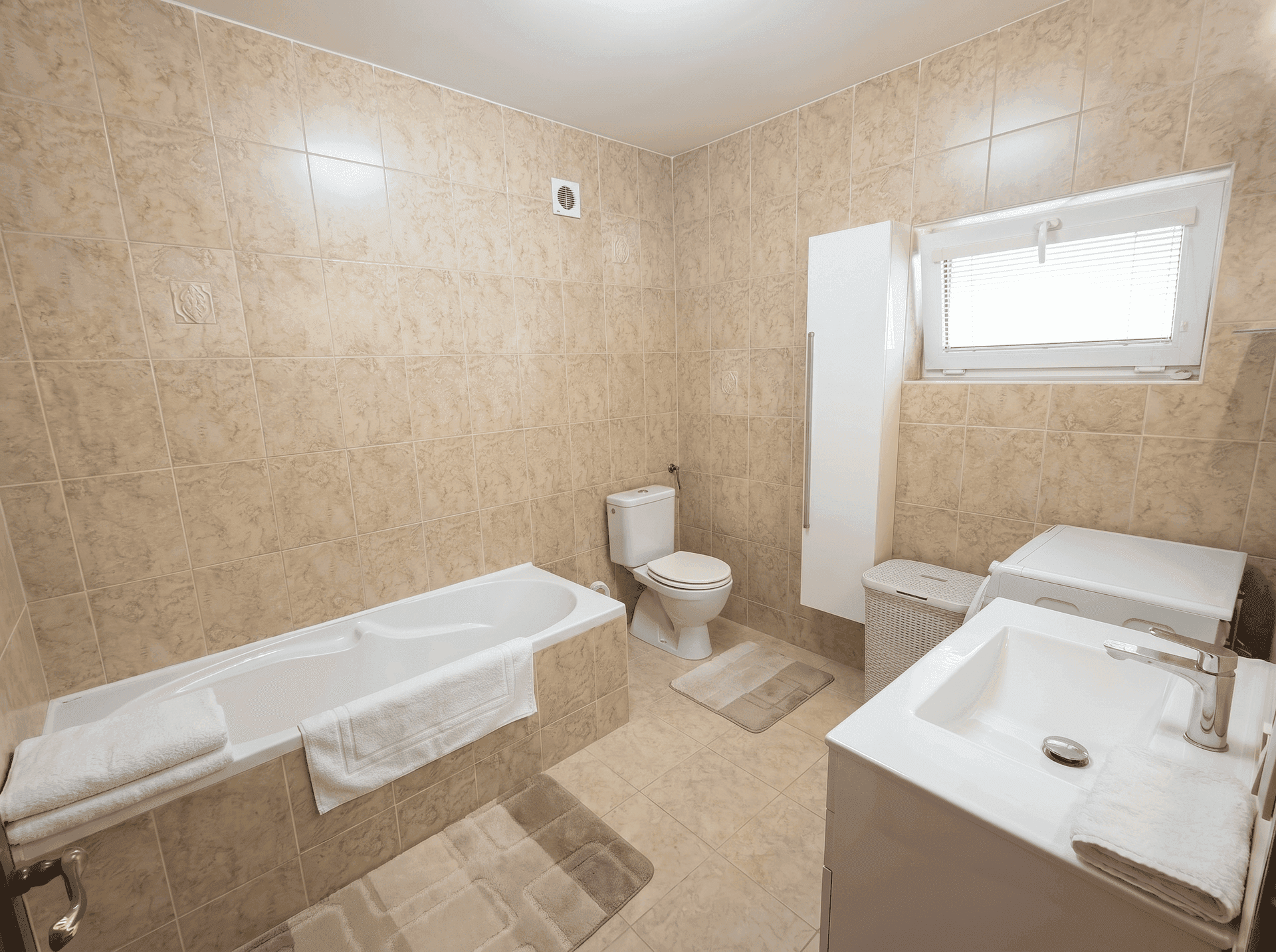 Gefliestes Badezimmer mit Badewanne, WC, Waschbecken und Fenster für Tageslicht.