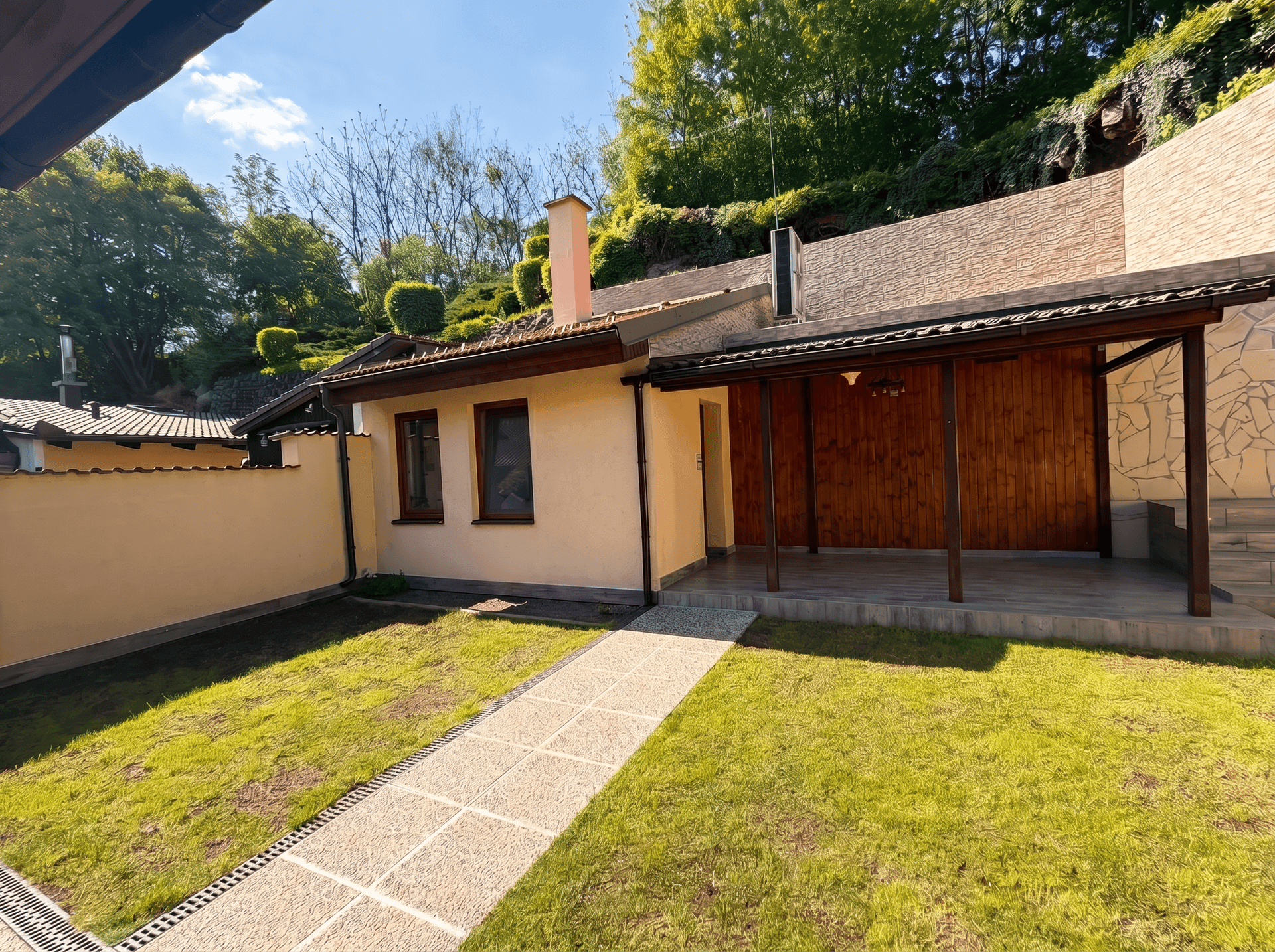 Sonnenbeschienener Garten mit Rasenfläche und überdachtem Sitzbereich am Haus.