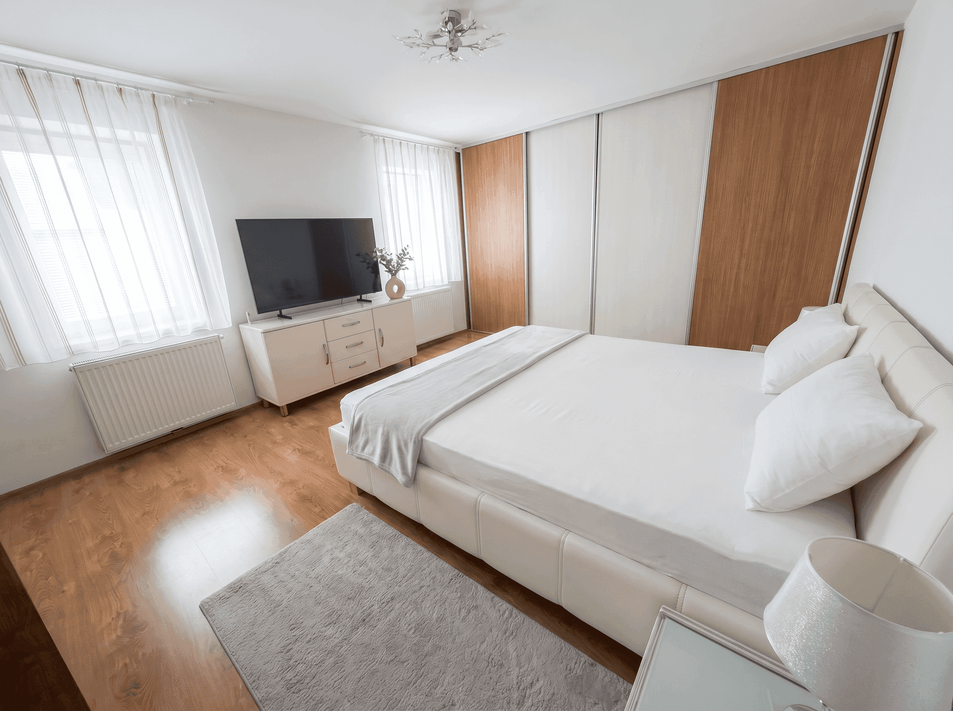 Modernes Schlafzimmer mit weißem Bett, TV-Möbel und Holzschränken.
