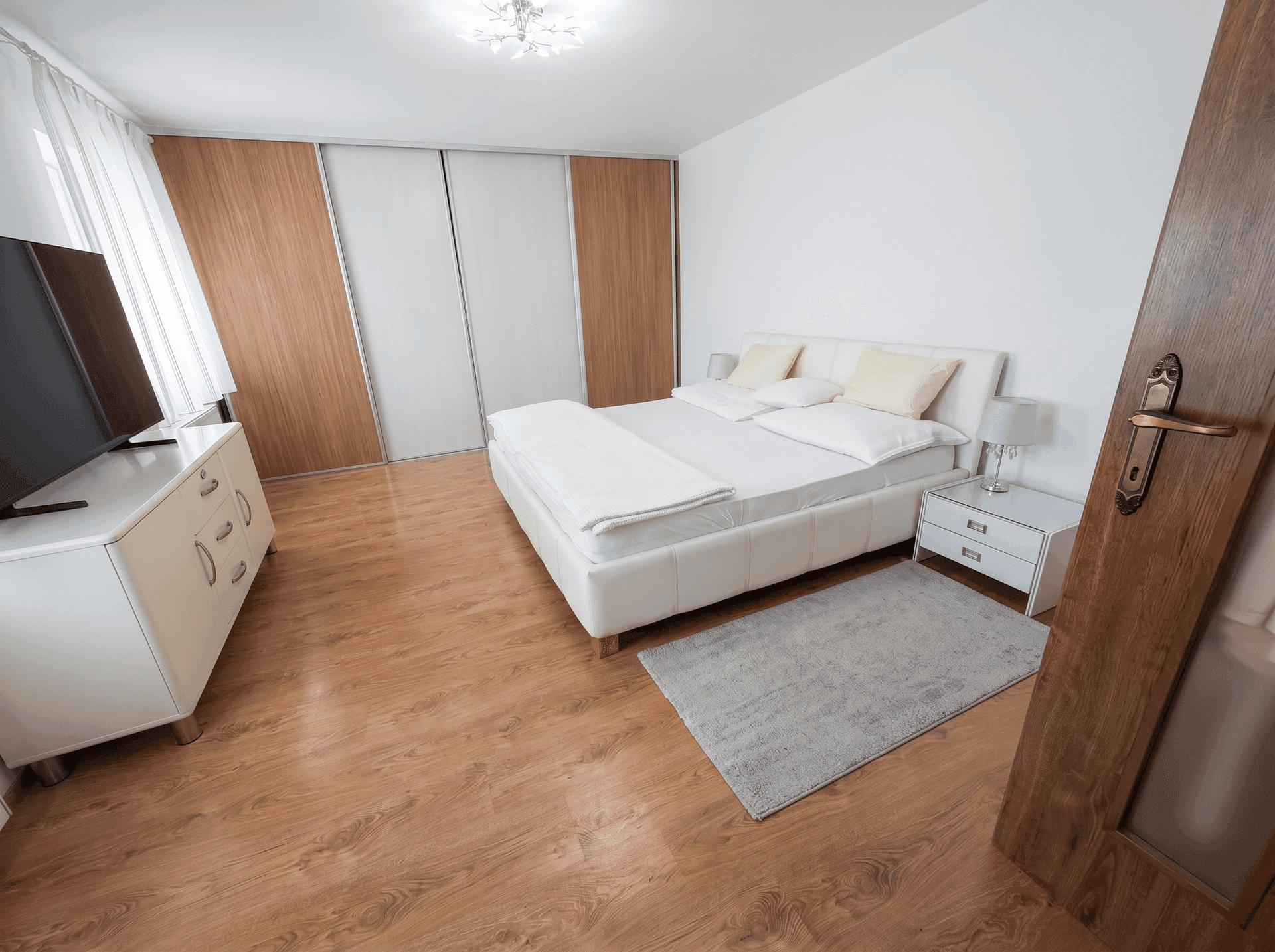 Helles Schlafzimmer mit weißem Bett, Holzboden und Zugang zu weiteren Räumen.