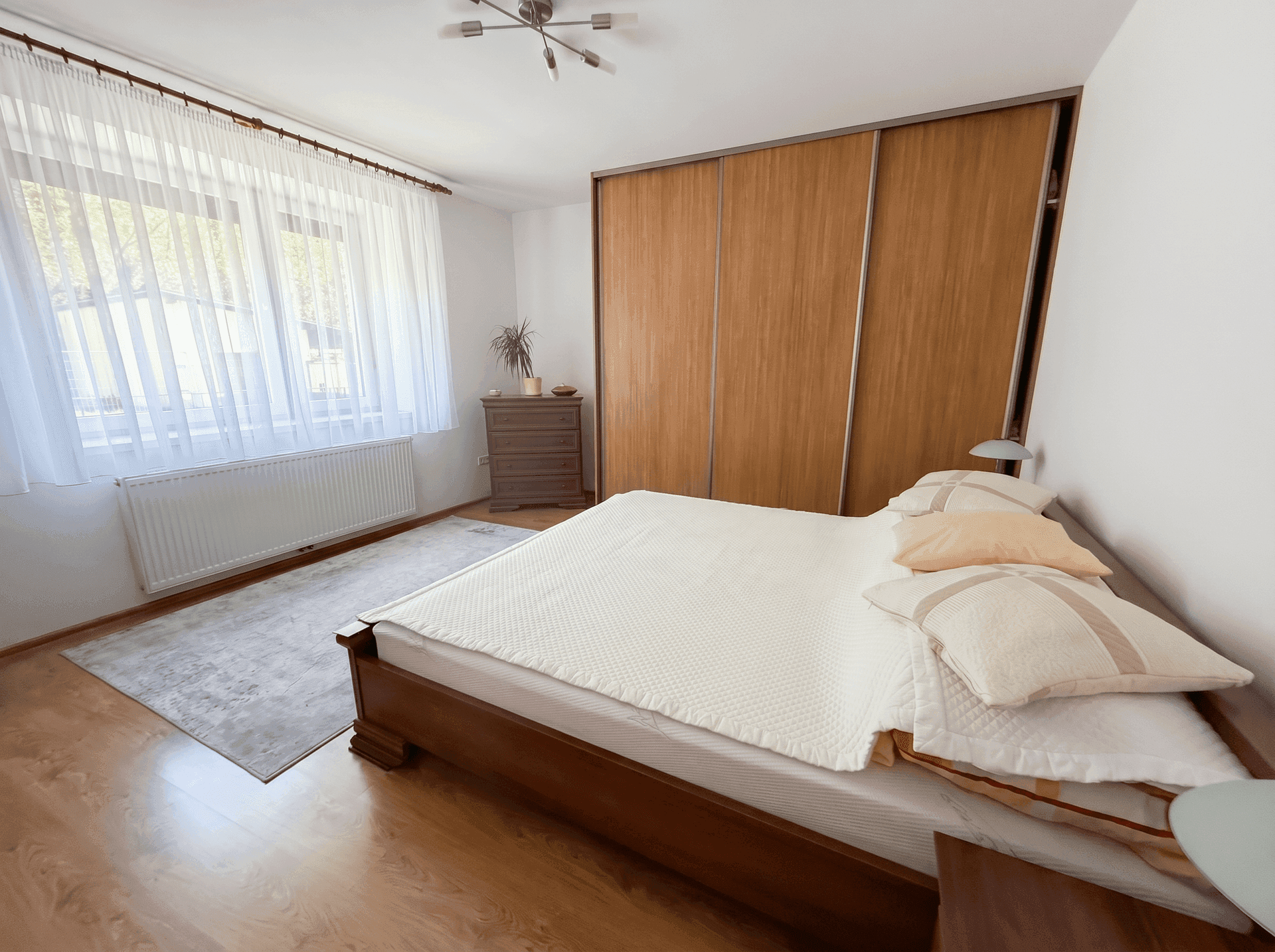 Helles Schlafzimmer mit großem Fenster, Holzboden und integrierten Schränken.