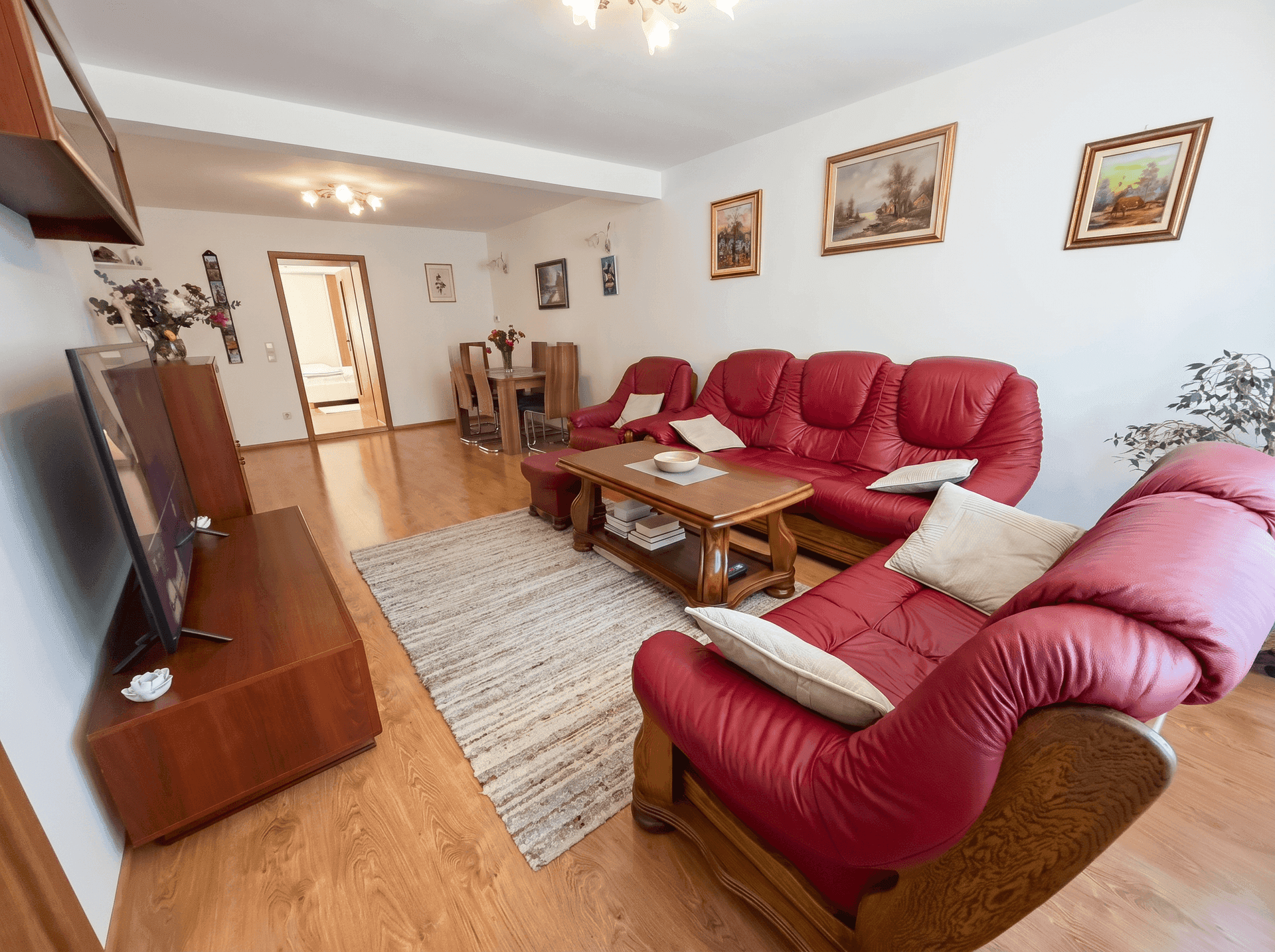 Geräumiges Wohnzimmer mit roten Ledersofas, Holzboden und TV-Bereich.