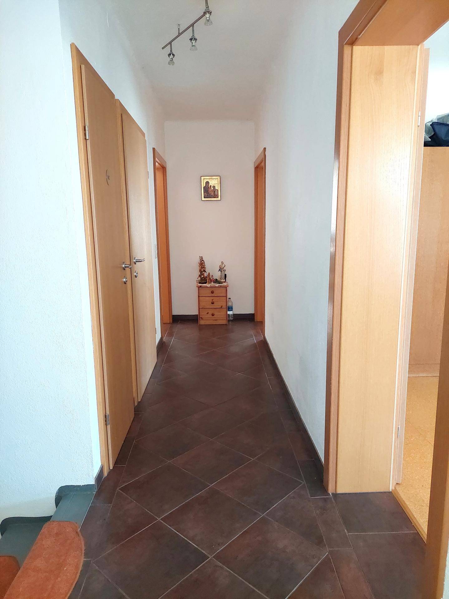 Langer Flur mit Fliesenboden und Holztüren, führt zu verschiedenen Zimmern.