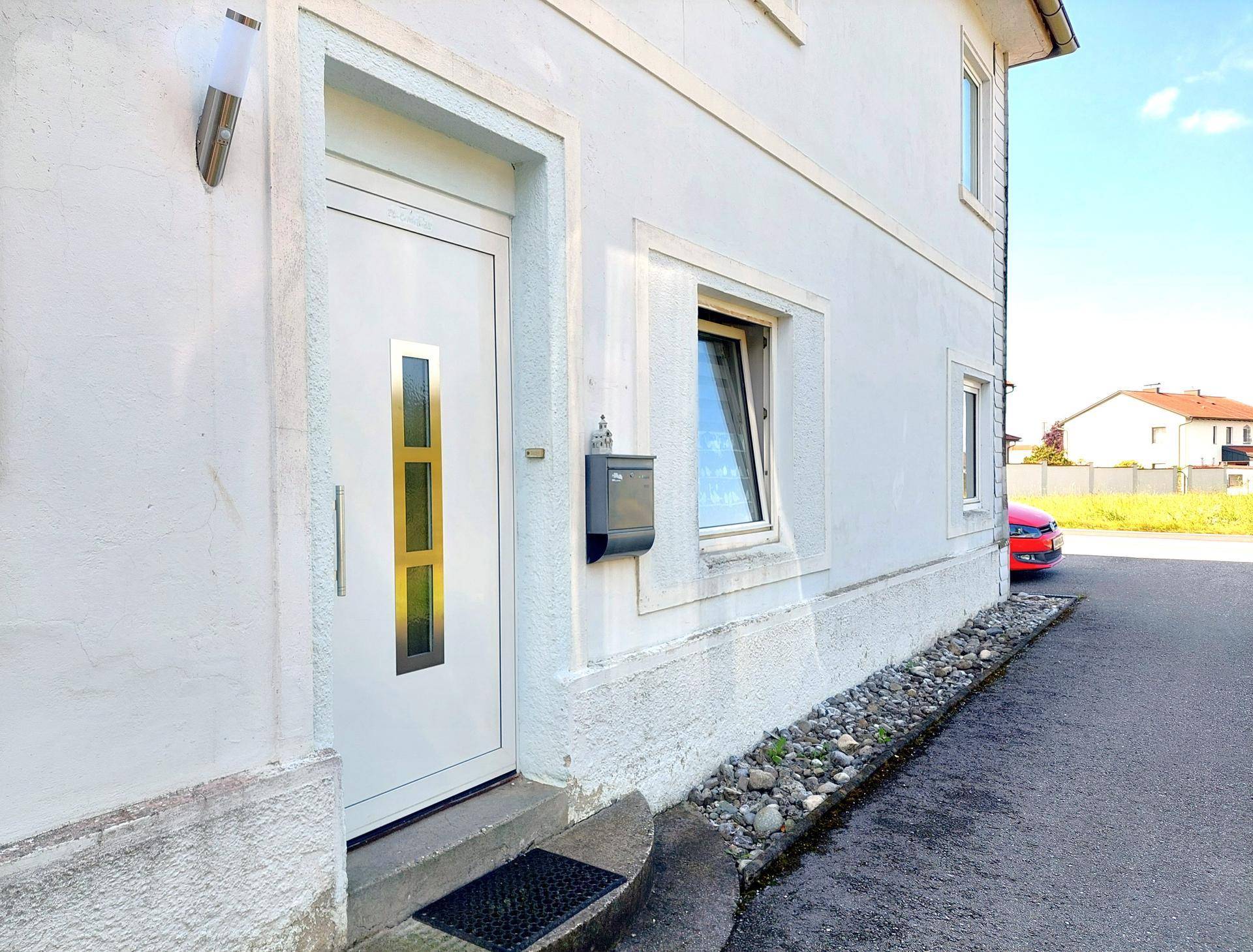 Eingangsbereich des Gebäudes mit weißer Tür und Fenster, umgeben von einer gepflegten Fassade.