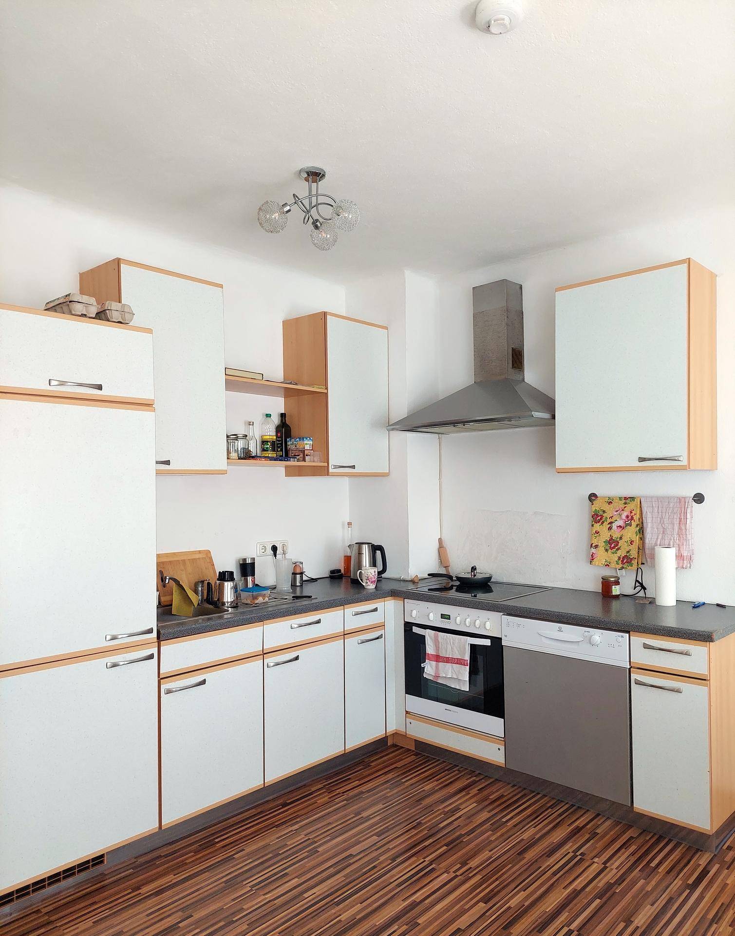 Funktionale Küche mit weißen Schränken, Holzdetails, Dunstabzugshaube und integrierten Geräten.