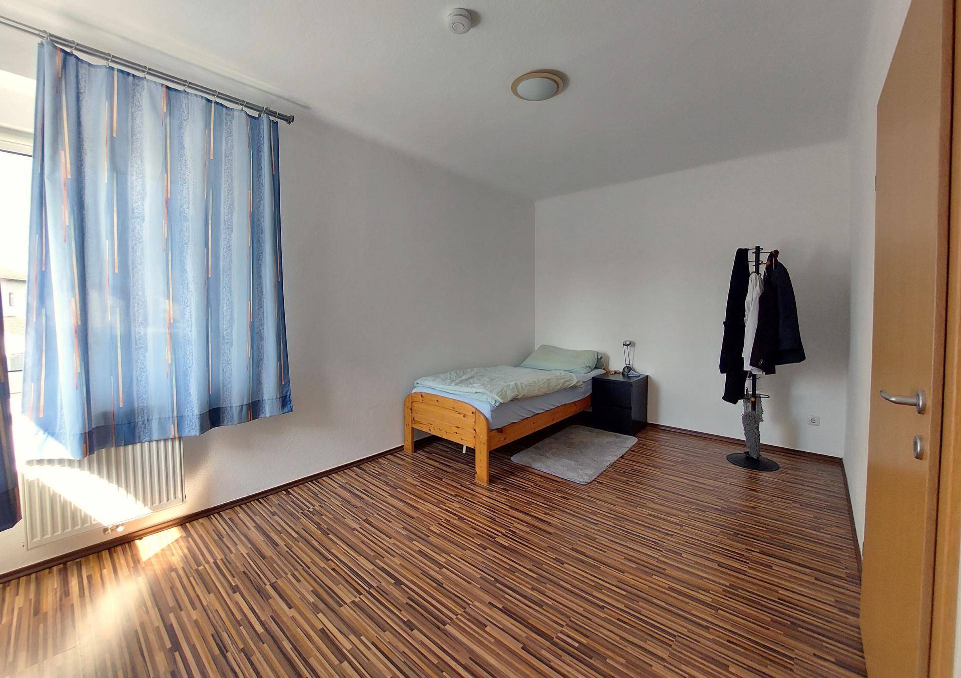 Einfaches Schlafzimmer mit Einzelbett und Kleiderständer, bietet ausreichend Platz.