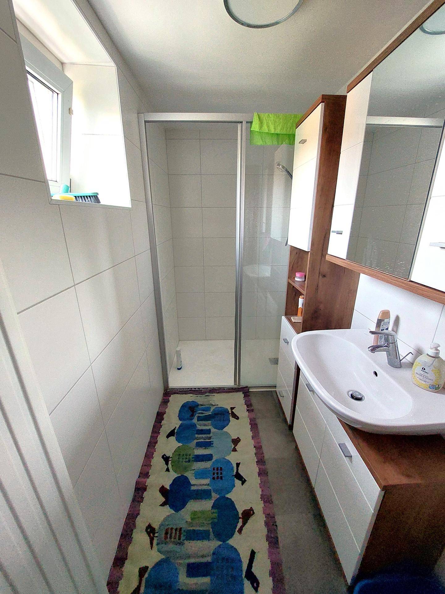 Modernes Badezimmer mit Duschkabine, Waschbecken und Spiegelschrank, hell gefliest.