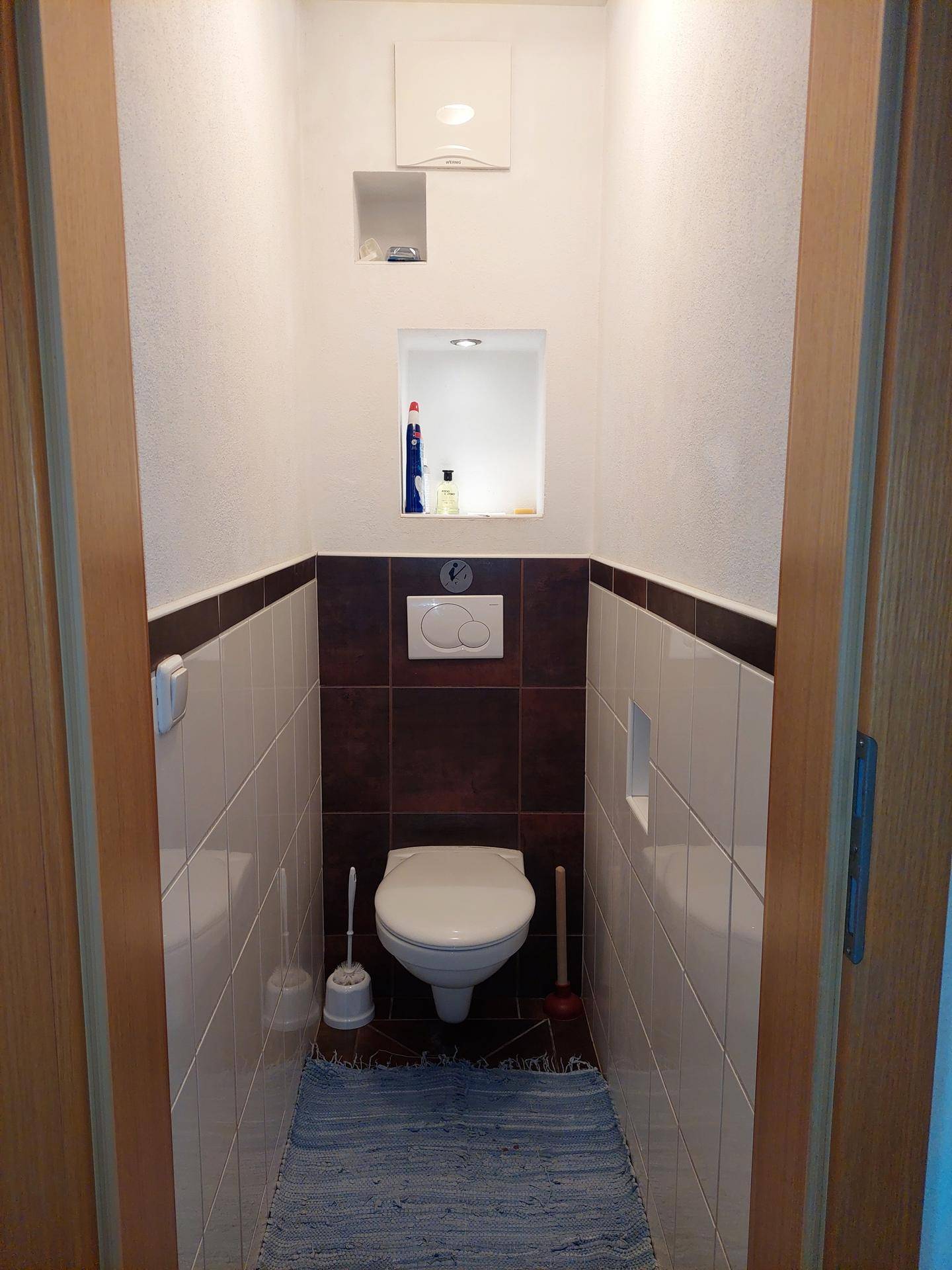 Separates WC mit Wandtoilette und Fliesen in Weiß und Braun, praktisch und funktional.