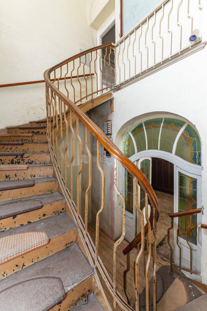 Historisches Treppenhaus mit geschwungener Treppe und einem farbigen Glasfenster im Eingangsbereich.