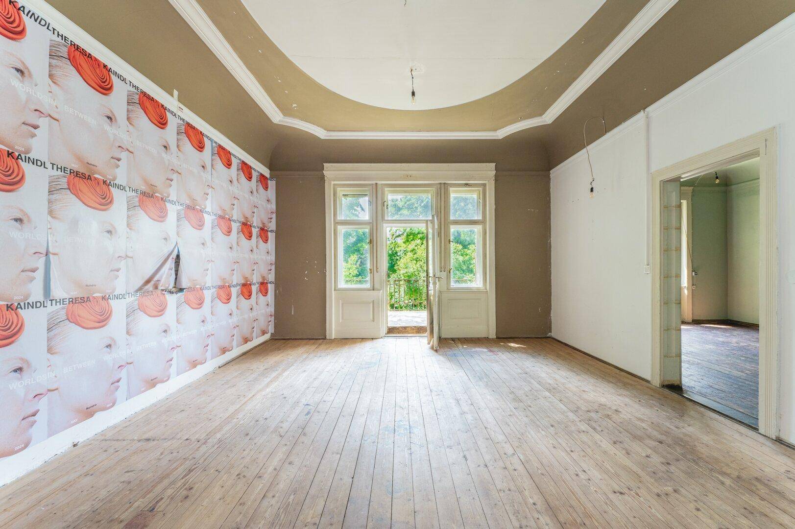 Helles Zimmer mit Holzboden, Stuckdecke und Zugang zu einem französischen Balkon mit Blick ins Grüne.