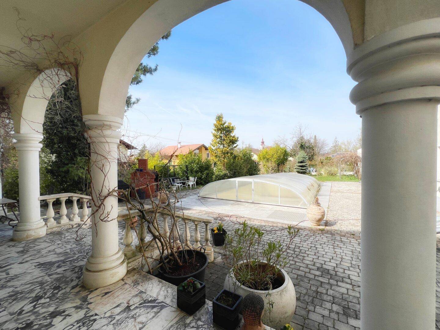 Überdachte Terrasse mit Marmorboden und Blick auf den Garten und den Poolbereich.