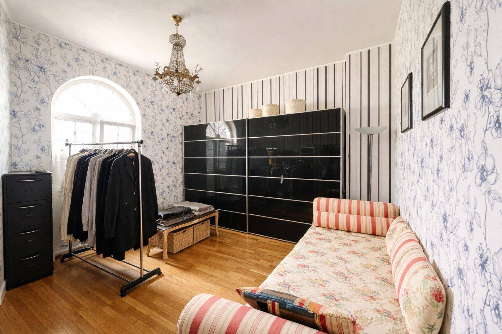 Schlafzimmer mit Holzboden, gemusterter Tapete und einem Kleiderständer für Kleidung.
