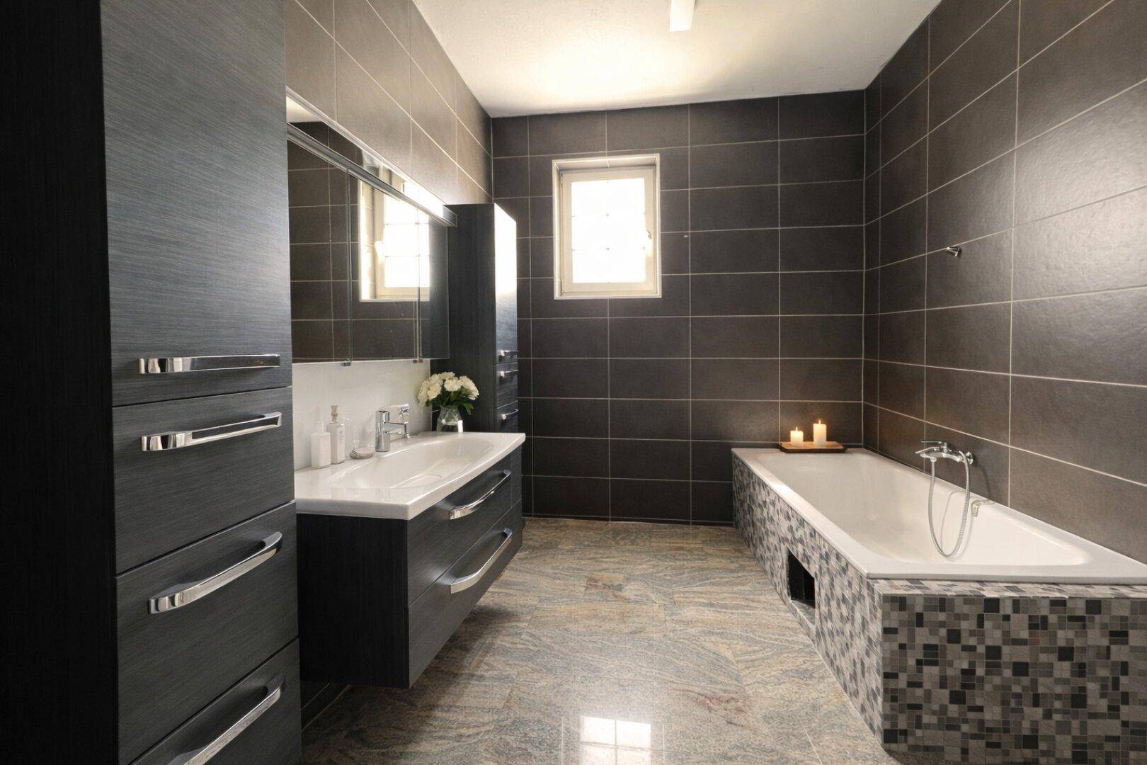 Modernes Badezimmer mit dunklen Fliesen, integrierter Badewanne und Einzelwaschbecken.