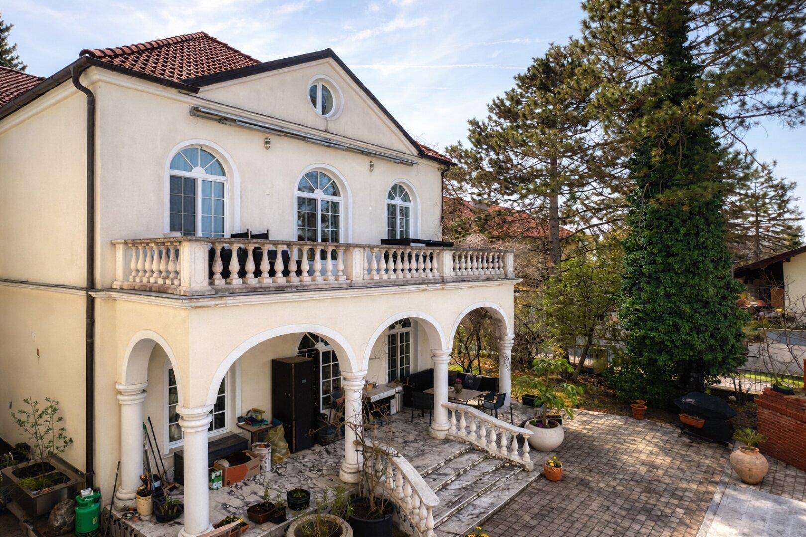 Seitliche Ansicht der Villa mit großem Balkon, Balustrade und Blick auf den Garten.