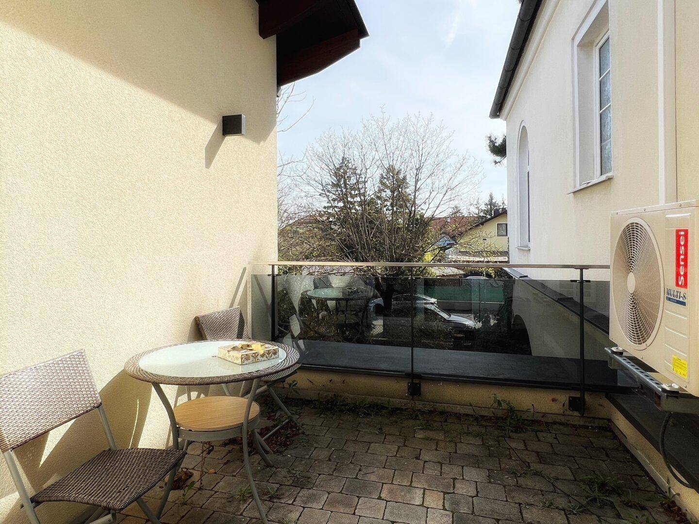 Kleiner Balkon mit Glasgeländer, Sitzgelegenheiten und Blick auf die Umgebung.