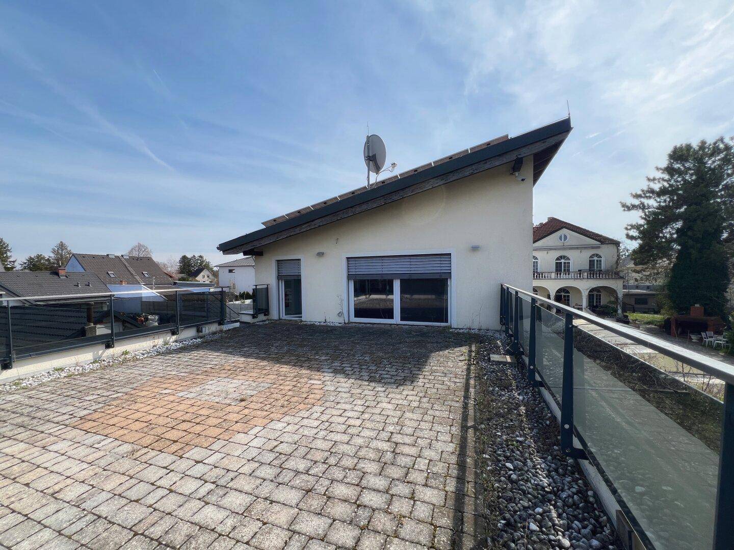 Geräumige Dachterrasse mit Pflastersteinen, Glasgeländer und weitem Blick.