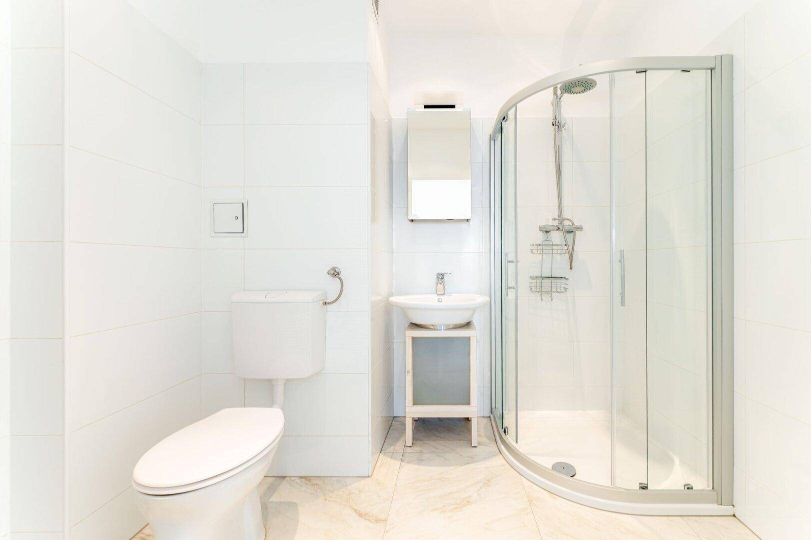 Modernes Badezimmer mit Duschkabine, WC und Waschbecken auf einem hellen Fliesenboden.