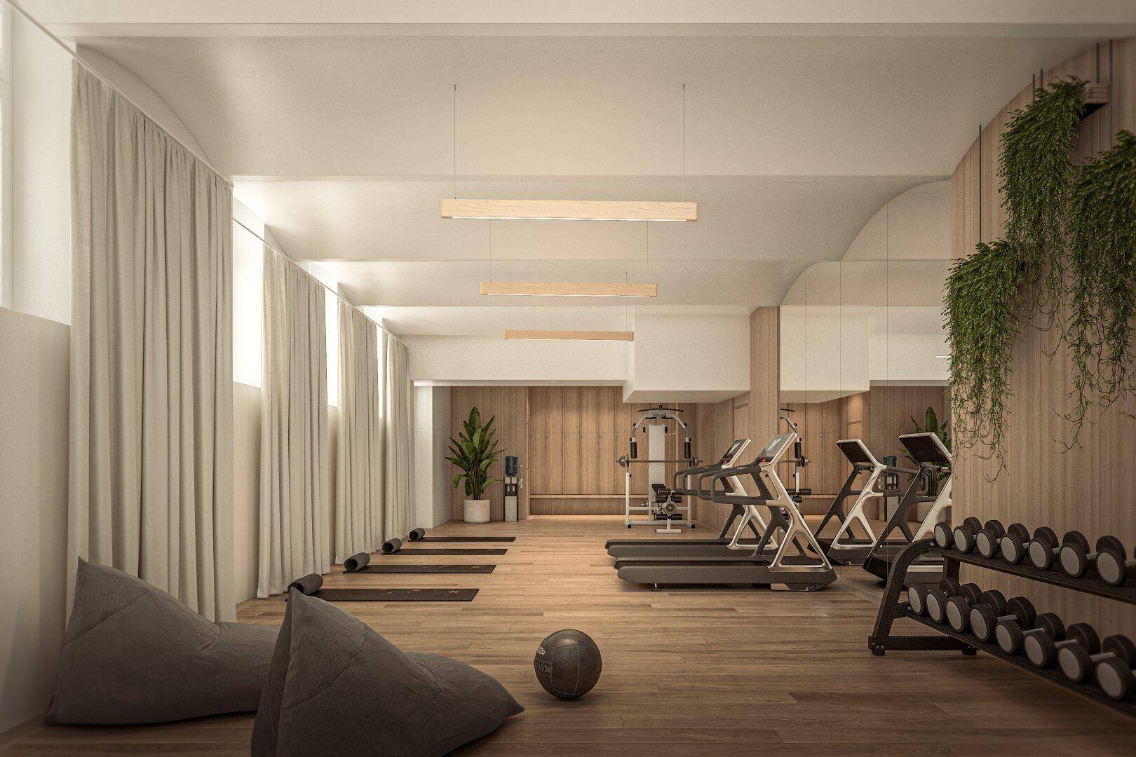 Geräumiger Fitnessraum mit modernen Trainingsgeräten, Holzboden, großen Fenstern und Spiegelflächen.