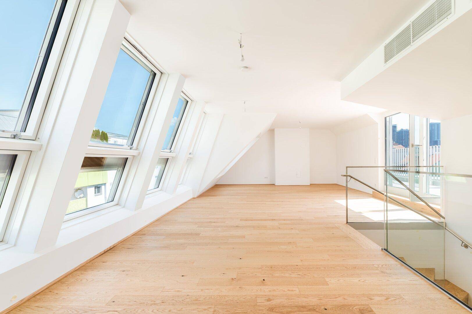 Helles Dachgeschosszimmer mit schrägen Fenstern, Holzboden und viel Tageslicht, ideal als Wohnbereich.