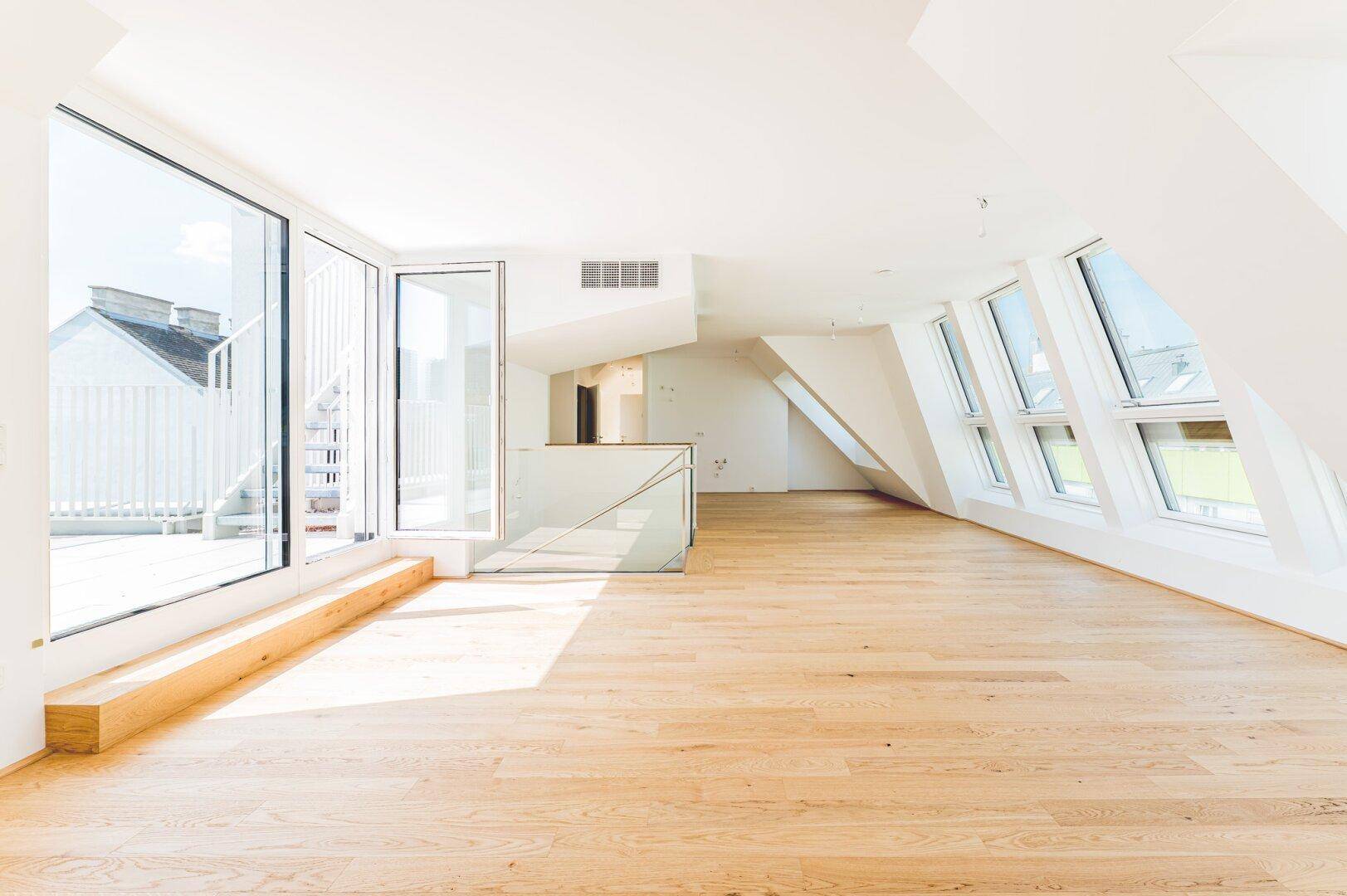 Lichtdurchfluteter Dachgeschossraum mit Holzboden und Zugang zu einer Terrasse, perfekt für offenes Wohnen.