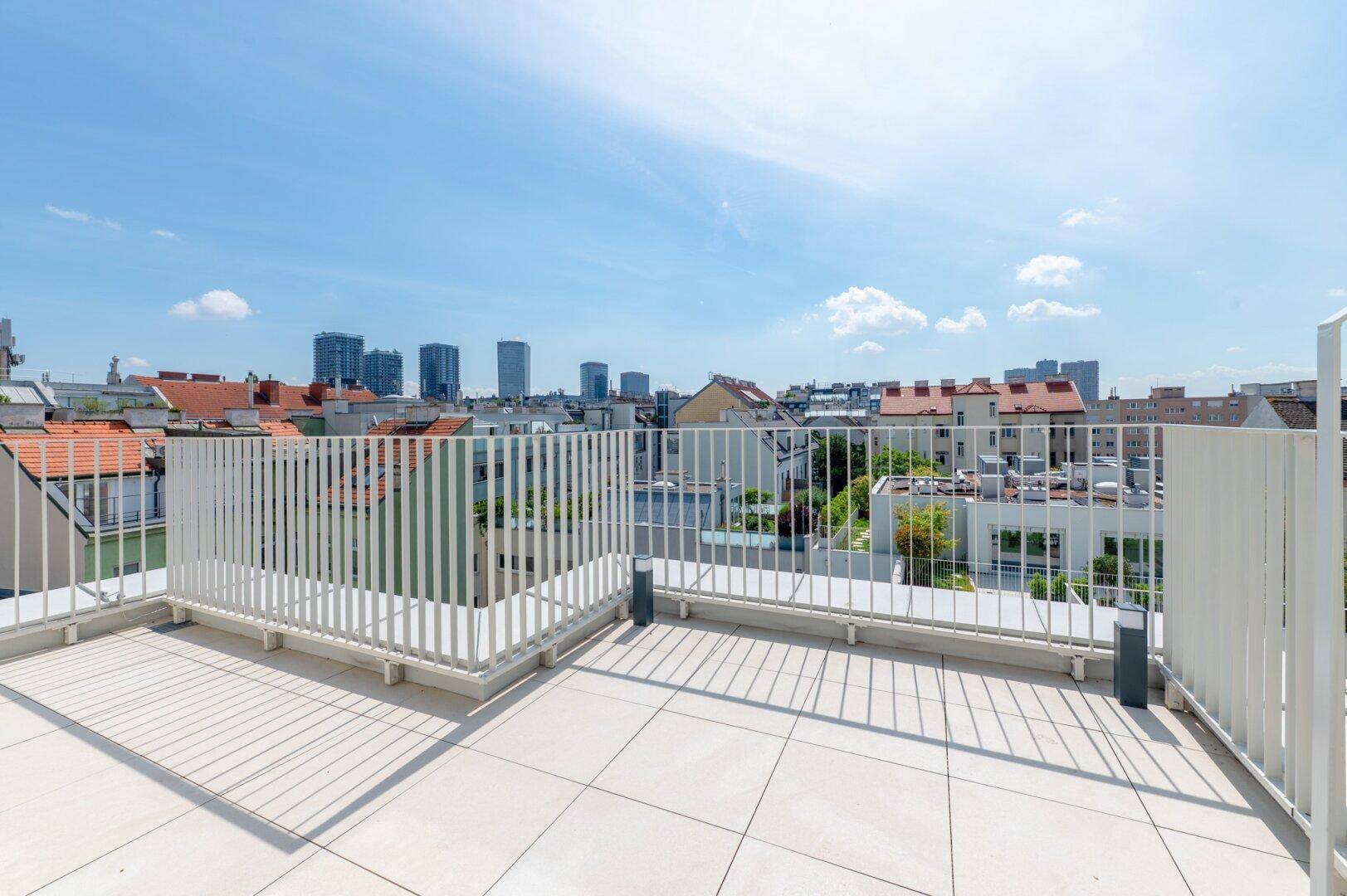 Geräumige Dachterrasse mit Fliesenboden und weitem Blick über die Stadt und umliegende Gebäude.