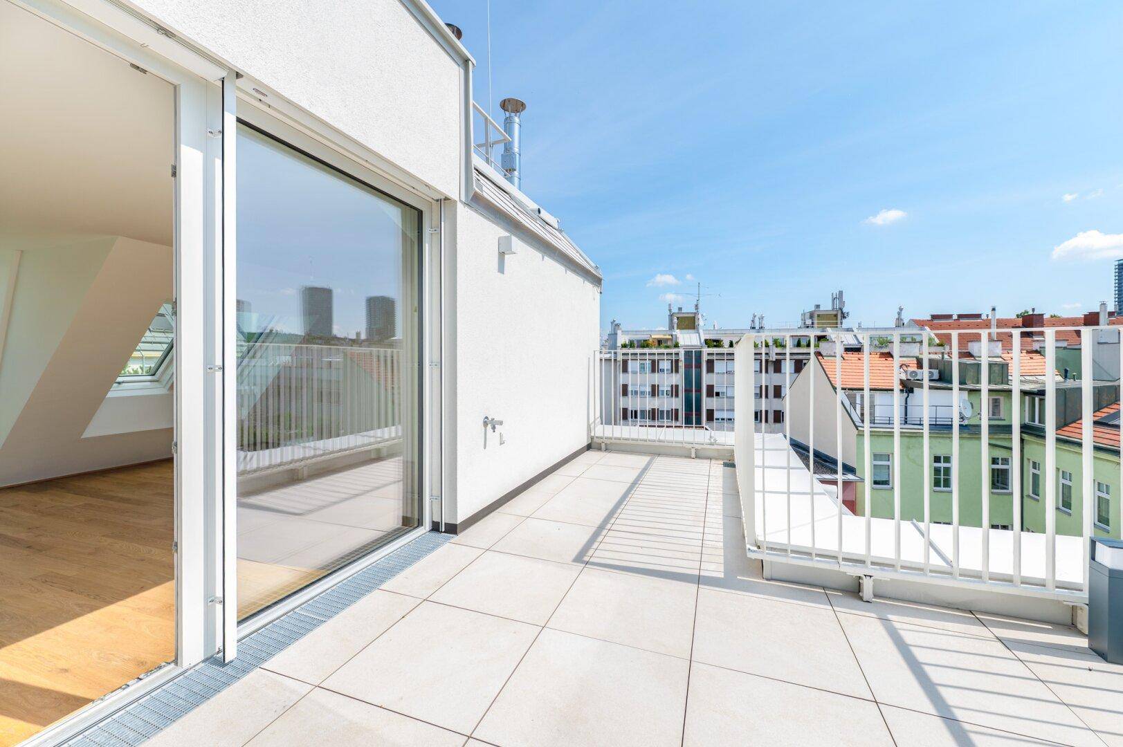 Sonniger Terrassenbereich mit Zugang zum Innenraum und Panoramablick auf die städtische Umgebung.