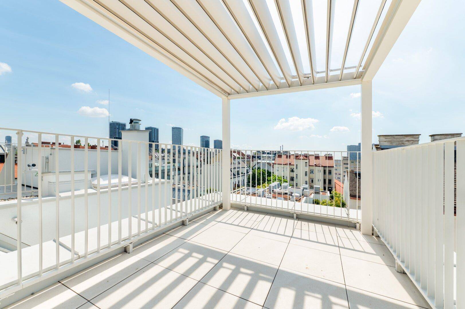Moderne Dachterrasse mit Pergola, Fliesenboden und beeindruckendem Stadtpanorama unter blauem Himmel.