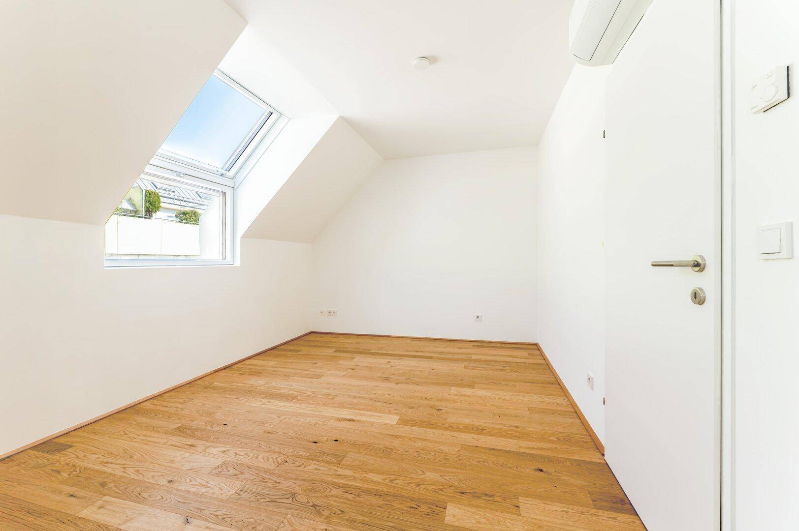 Gemütliches Schlafzimmer mit Holzboden, Dachfenster und Klimaanlage, ideal für erholsame Nächte.
