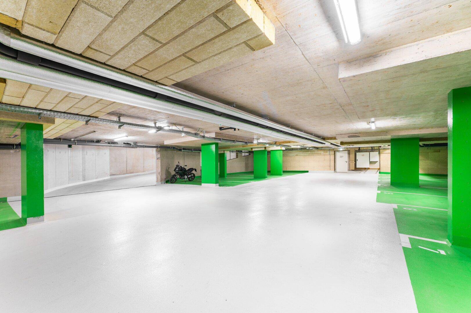 Geräumige Tiefgarage mit hellen Stellplätzen und markanten grünen Säulen und Bodenmarkierungen.