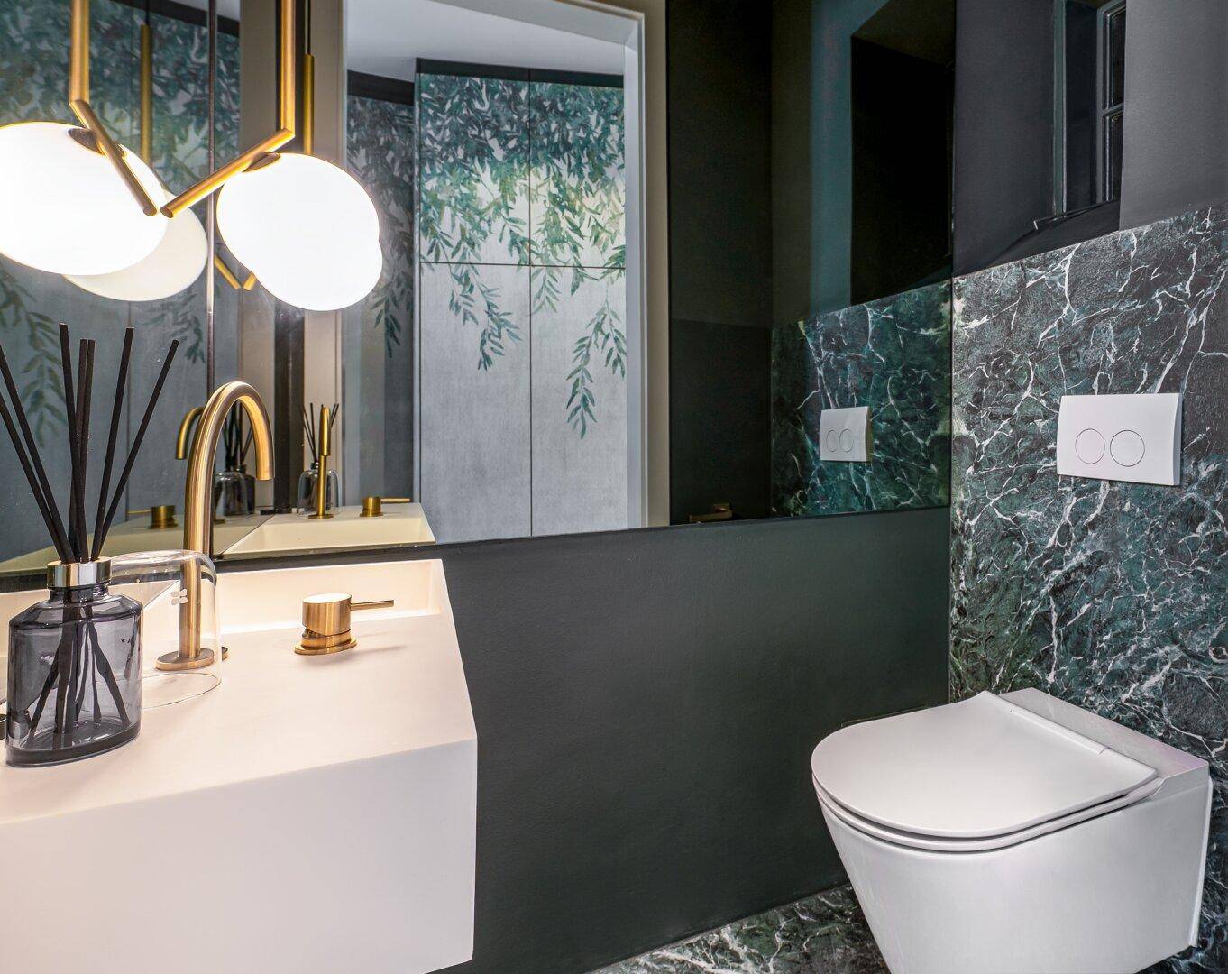 Modernes WC mit wandhängender Toilette, stilvollem Waschbecken und goldenen Armaturen.