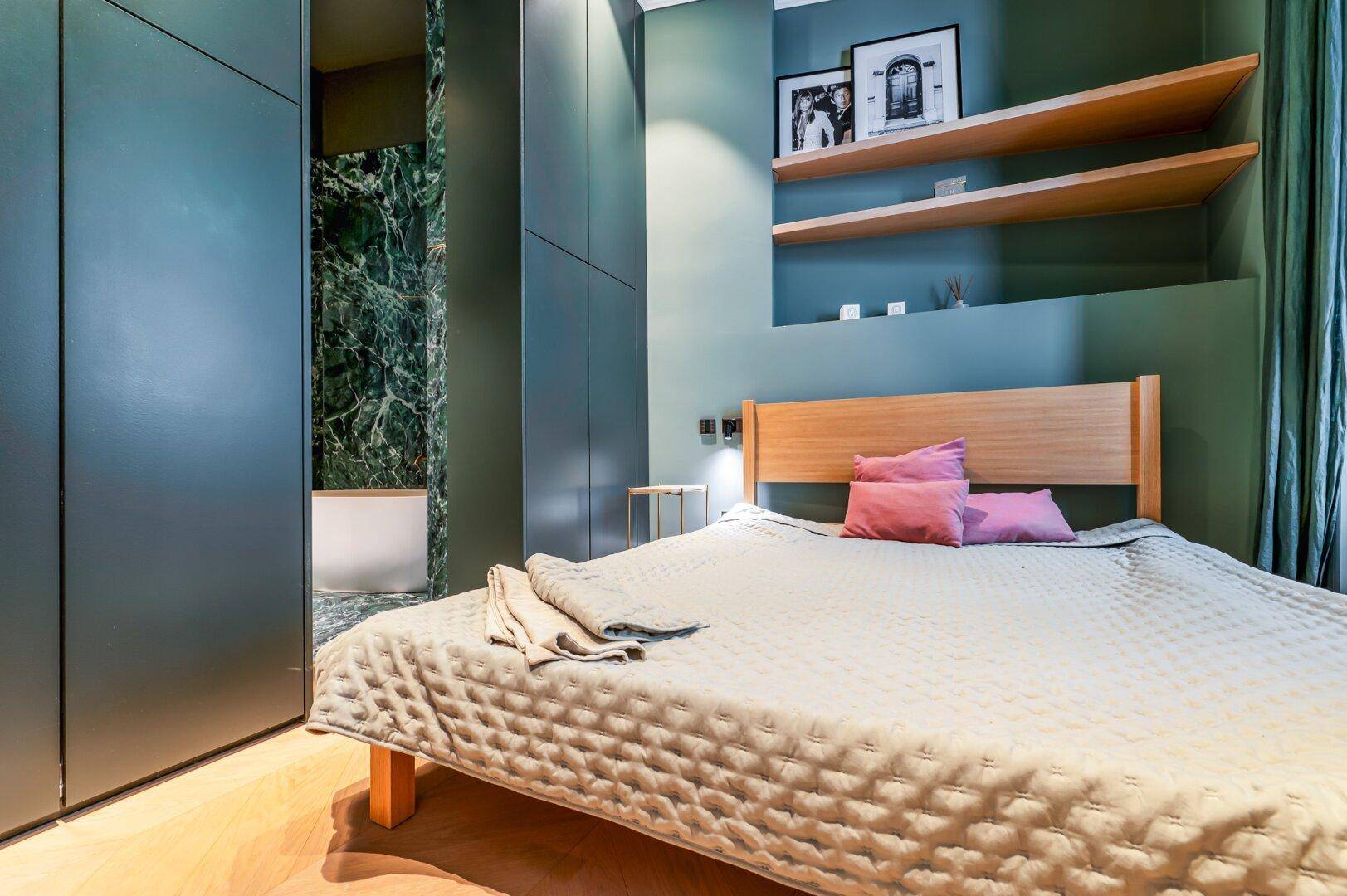 Schlafzimmer mit Holzbett, integrierten Schränken und direktem Zugang zu einem Marmorbad.