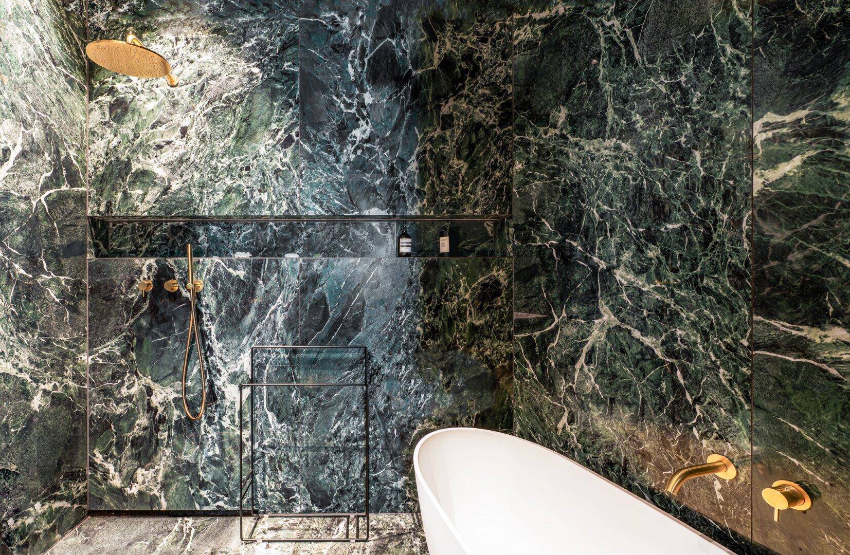 Luxuriöses Badezimmer mit dunkelgrünen Marmorwänden, freistehender Badewanne und goldenen Armaturen.