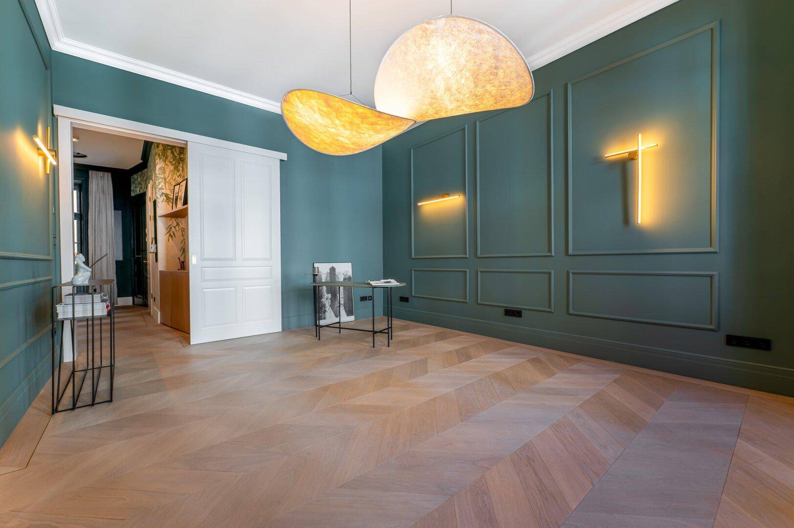 Helles Zimmer mit grünen Wandpaneelen, Fischgrätparkett und einer eleganten Schiebetür.