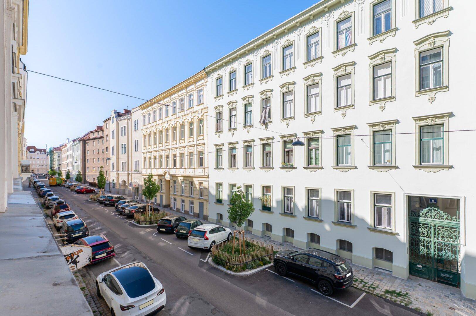 Historische Fassade eines Wohngebäudes an einer belebten Straße mit parkenden Autos.