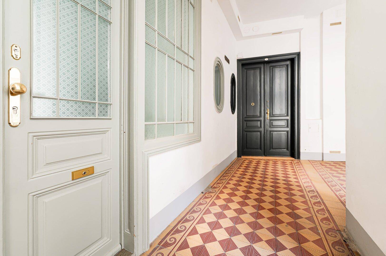 Eingangsbereich mit gemustertem Fliesenboden, weißer Eingangstür und dunkler Innentür.