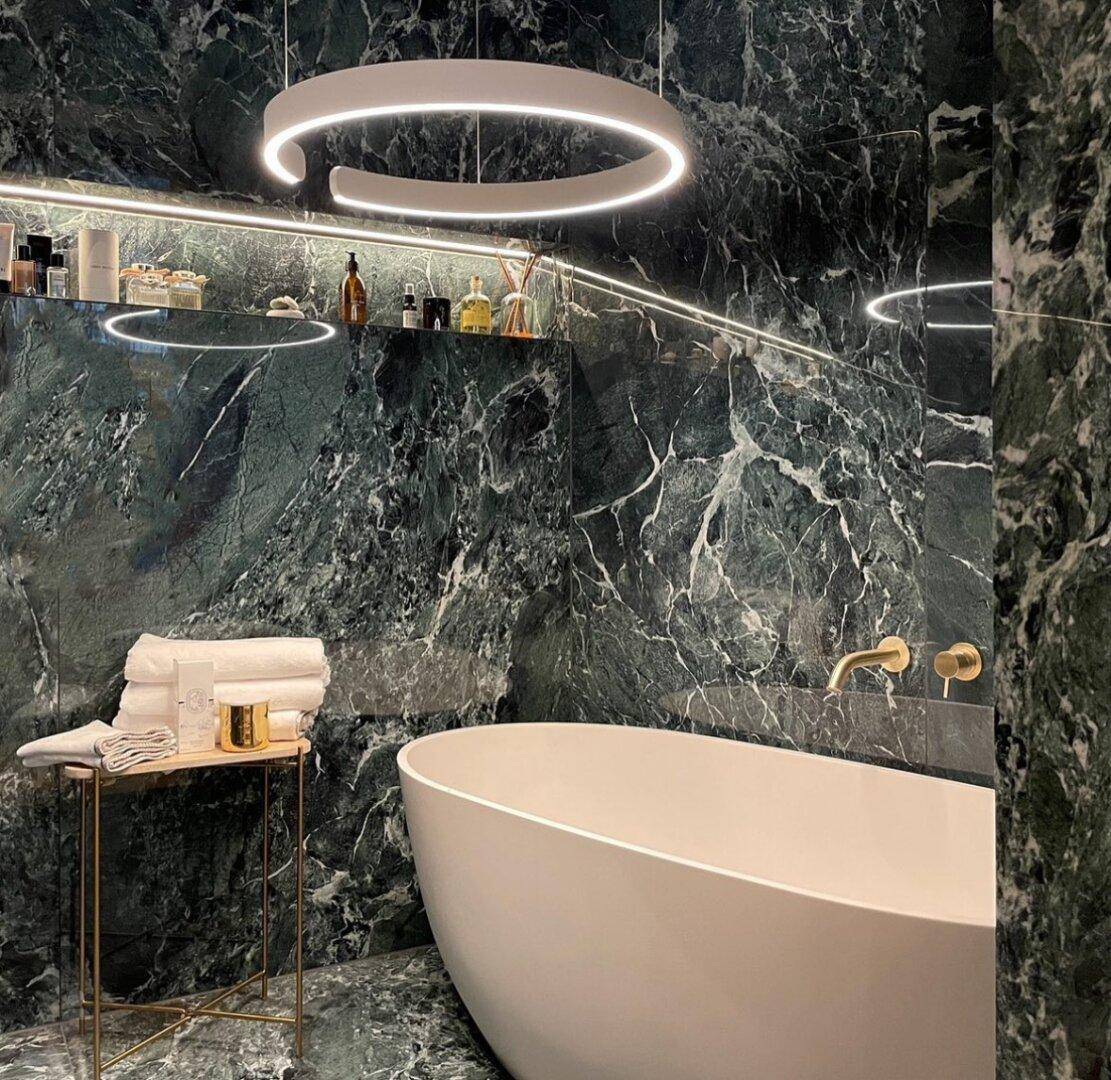 Elegantes Badezimmer mit dunkelgrünen Marmoroberflächen, freistehender Badewanne und moderner Beleuchtung.