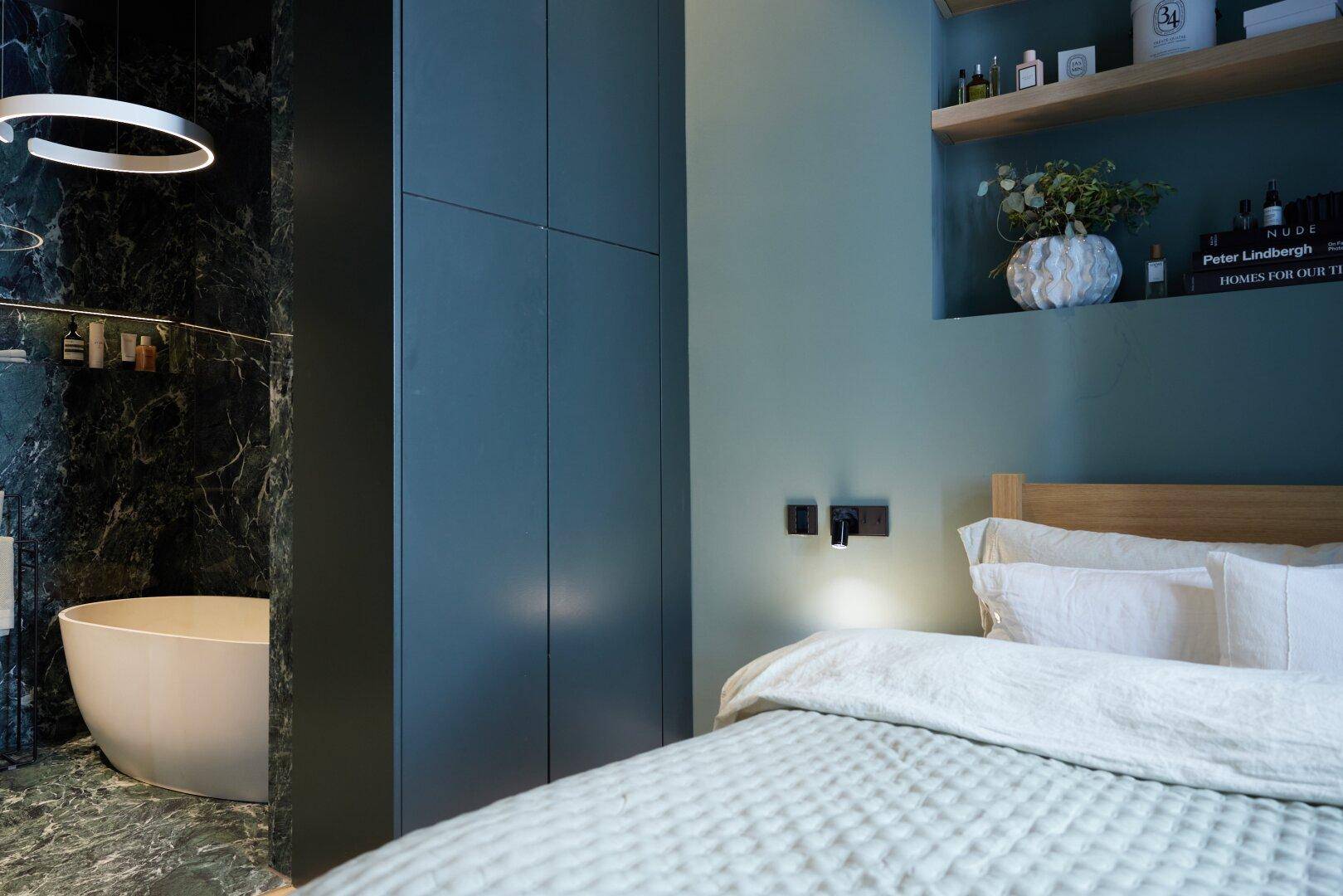 Schlafzimmer mit Holzbett, Einbauschränken und Blick auf eine freistehende Badewanne im angrenzenden Bad.