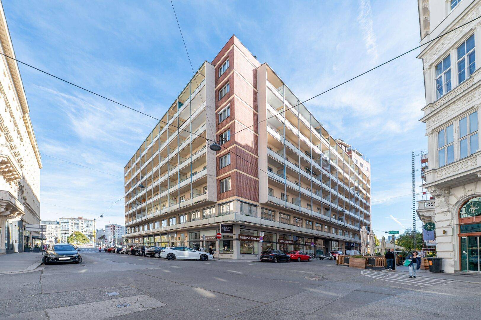 Großes, modernes Wohngebäude an einer Straßenecke mit vielen Balkonen und Geschäften im Erdgeschoss.