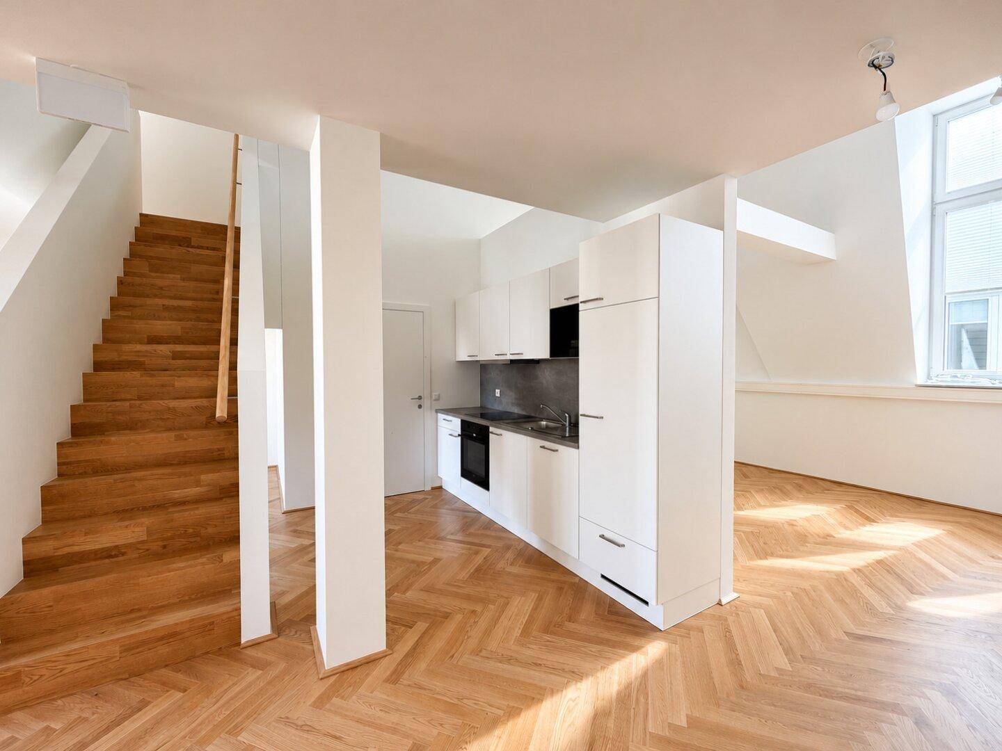 Moderne Küchenzeile in einem offenen Wohnbereich mit Fischgrätparkett und Holztreppe.