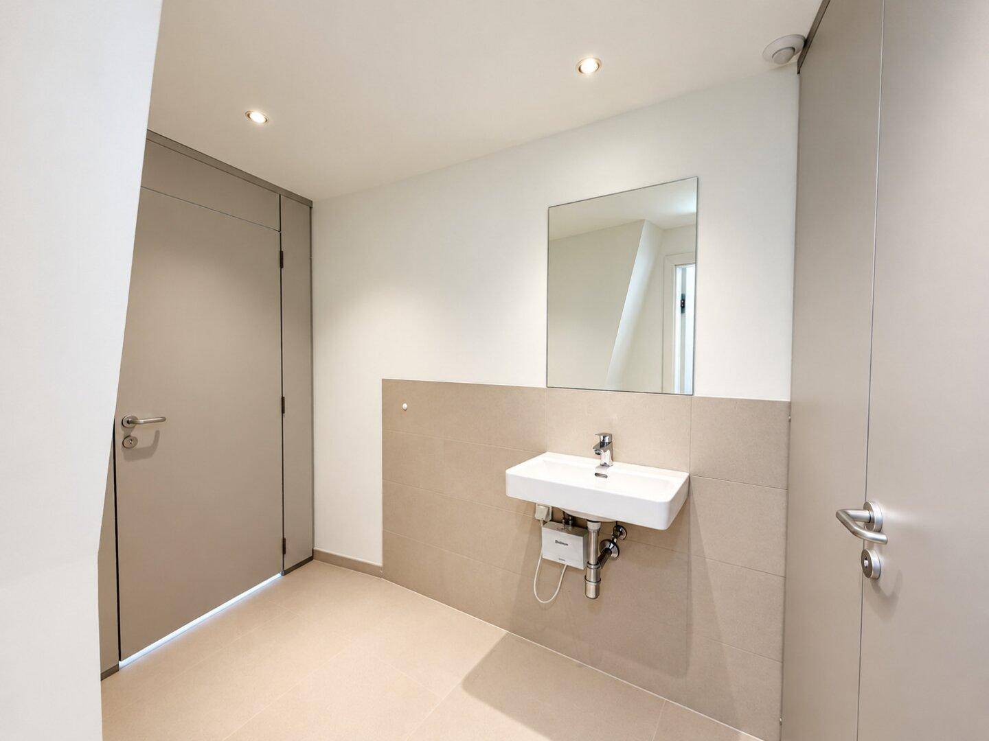 Modernes Badezimmer mit Waschbecken, Spiegel und hellen Fliesen an den Wänden.