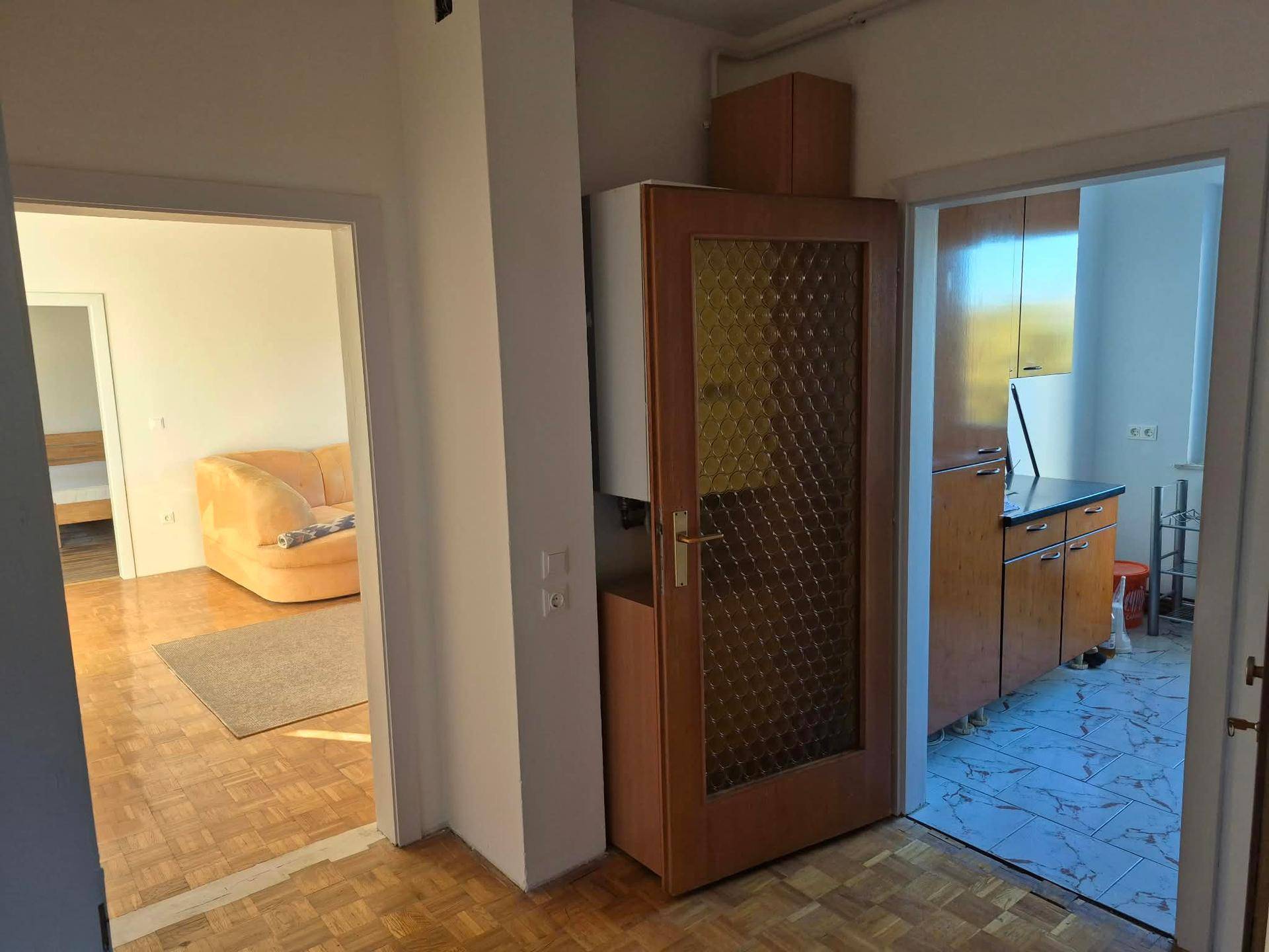 Flur mit Holzboden, der den Zugang zu einem Wohnzimmer und einer Küche ermöglicht.