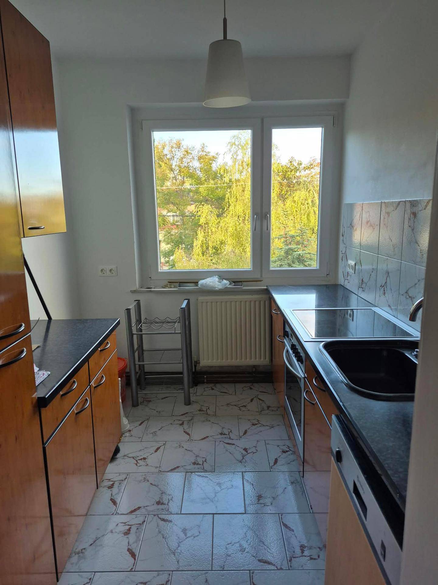 Funktionale Küche mit Holzschränken, dunklen Arbeitsplatten und einem Fenster mit Blick ins Grüne.