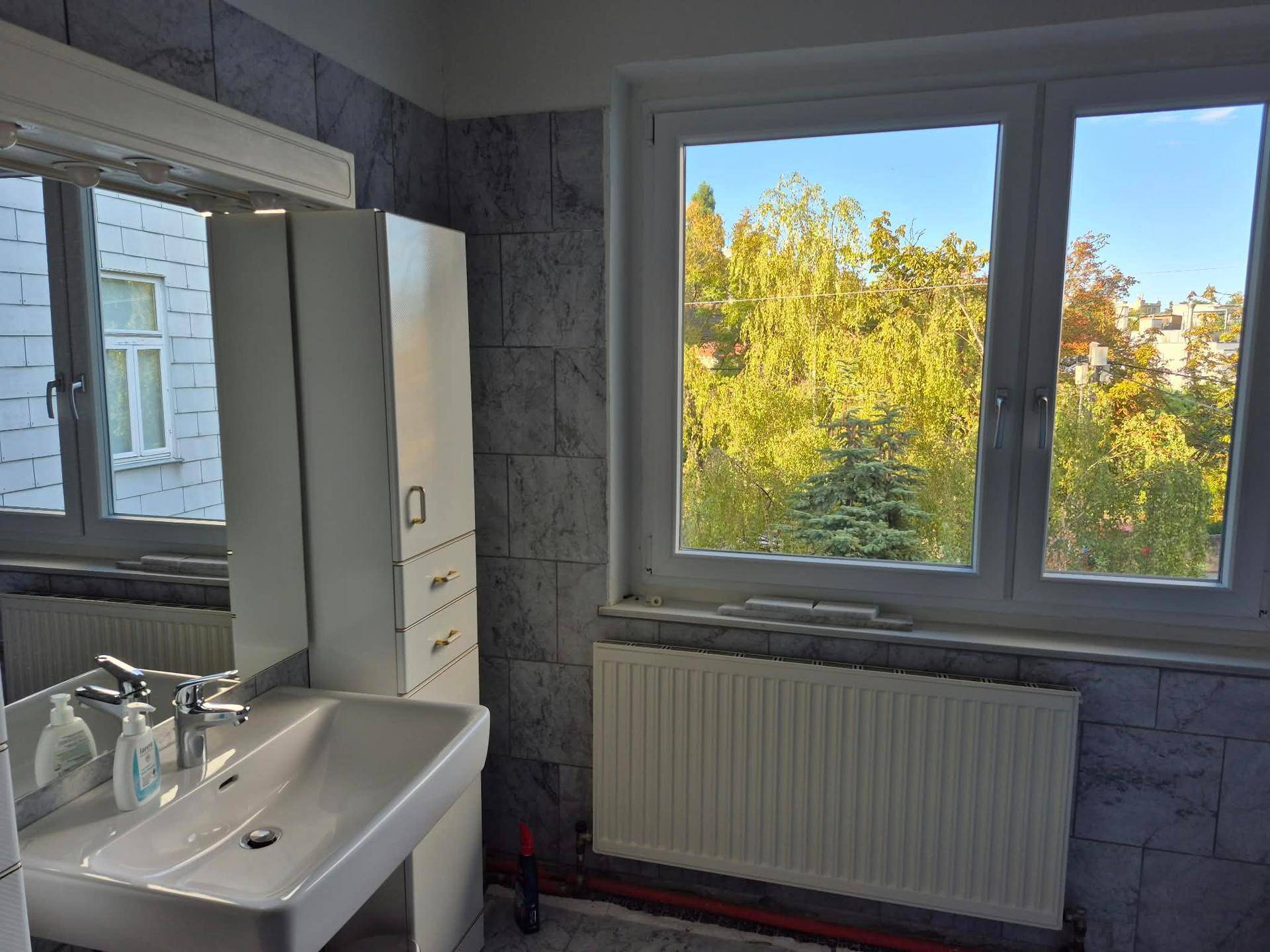 Helles Badezimmer mit Waschbecken, Spiegelschrank, gefliesten Wänden und großem Fenster mit Grünblick.