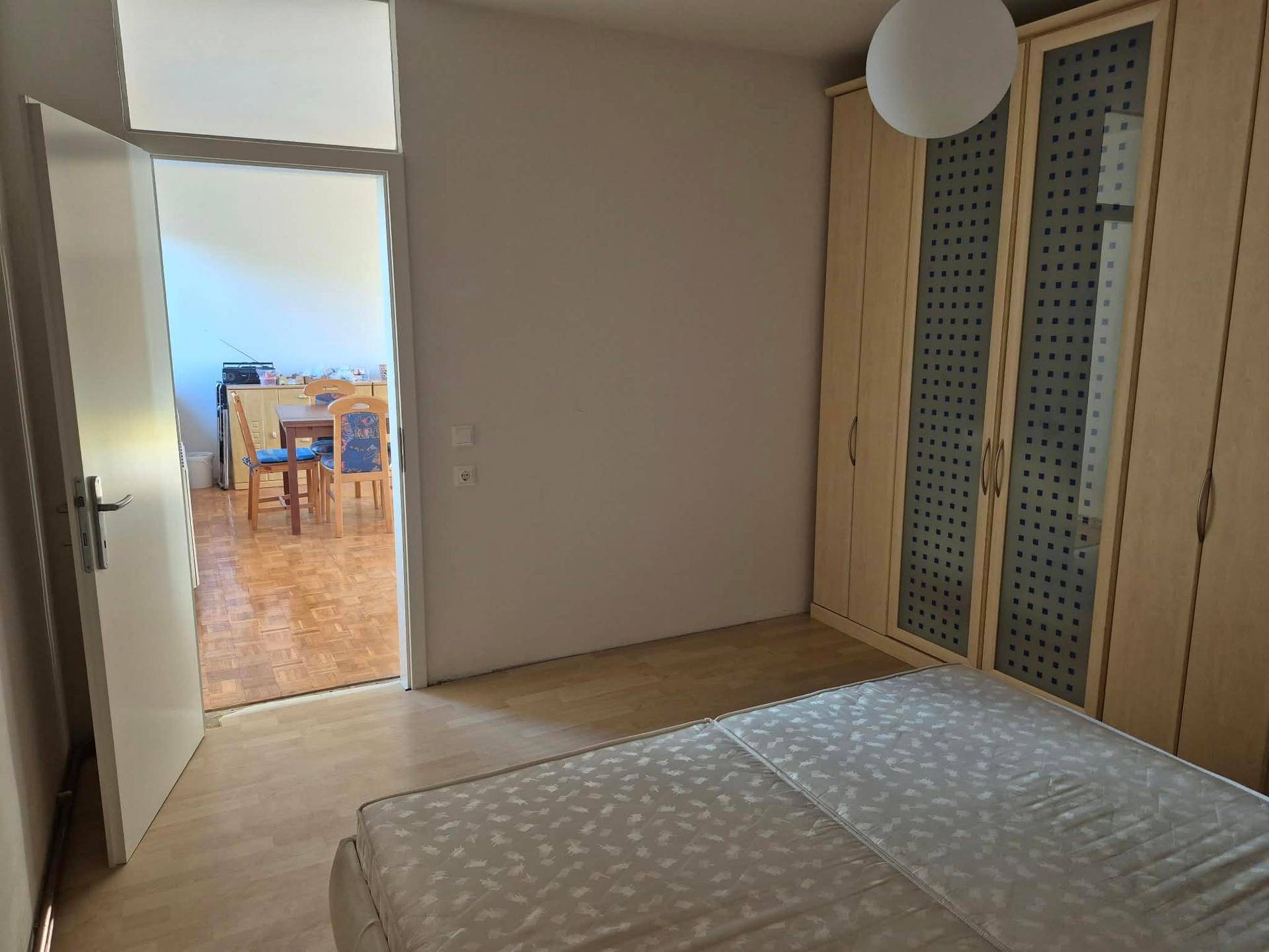 Schlafzimmer mit Bett und Kleiderschrank, das durch eine offene Tür mit dem Essbereich verbunden ist.